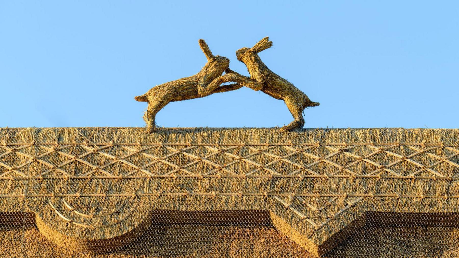 Two straw boxing hares pictured sitting on the barn's roof