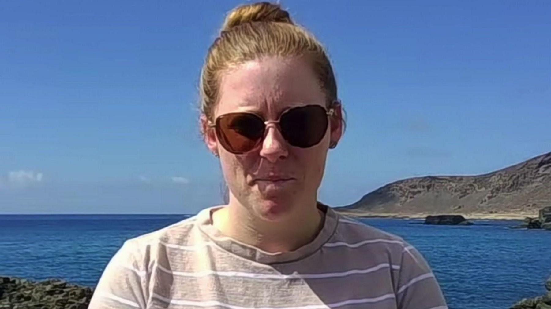 Nikita Goddard on the coast of  Gran Canaria with blue sea and coastline behind her