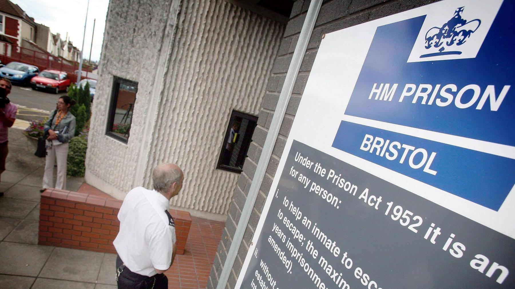 A prison officer walks into the entrance of HMP Bristol, under a sign welcoming people to the site