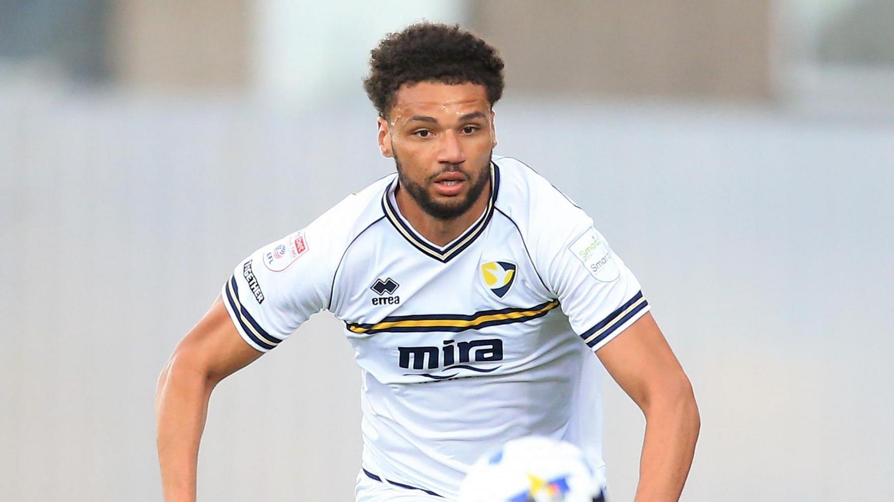 Lee Angol runs after the ball as it bounces in front of him during a match for Cheltenham