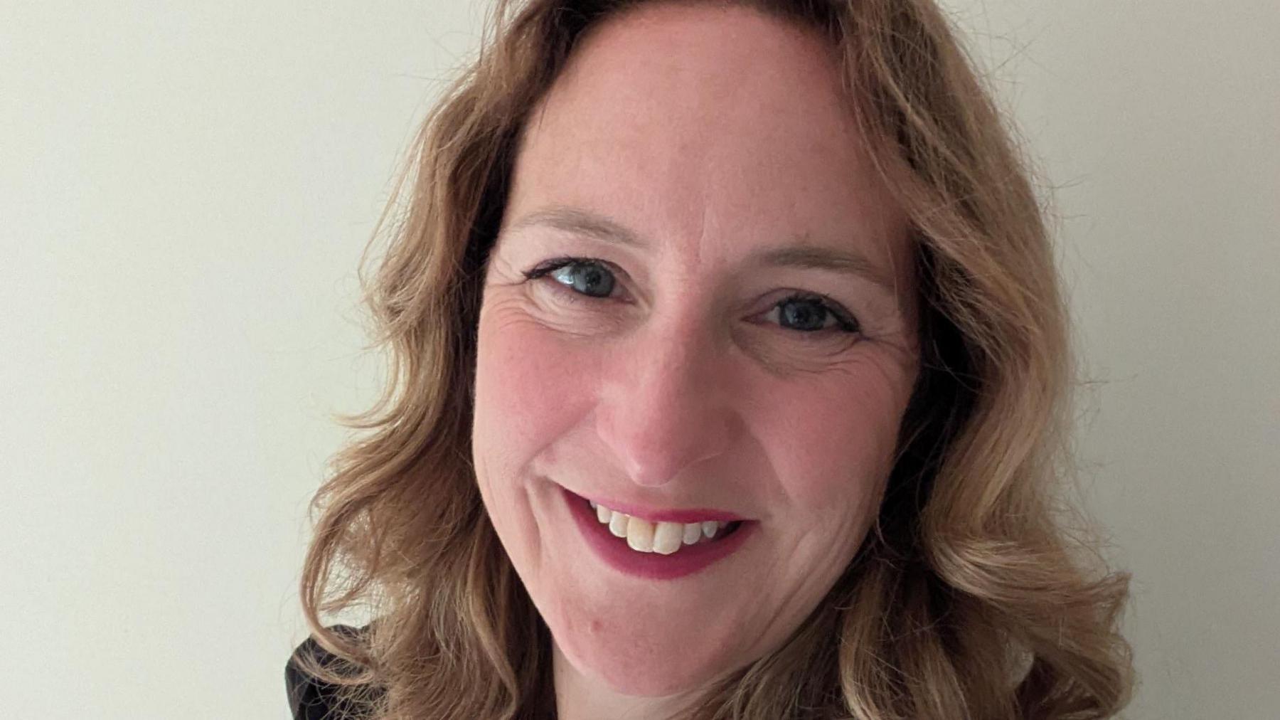 A woman with short curly hair and red lipstick is smiling. 