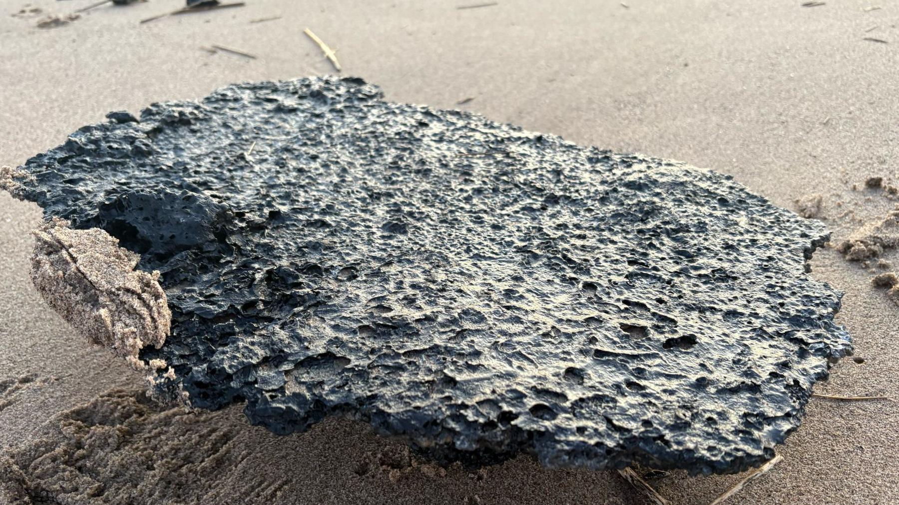 A burnt black clump of what appears to be plastic pellets on the beige coloured sand at Skegness.