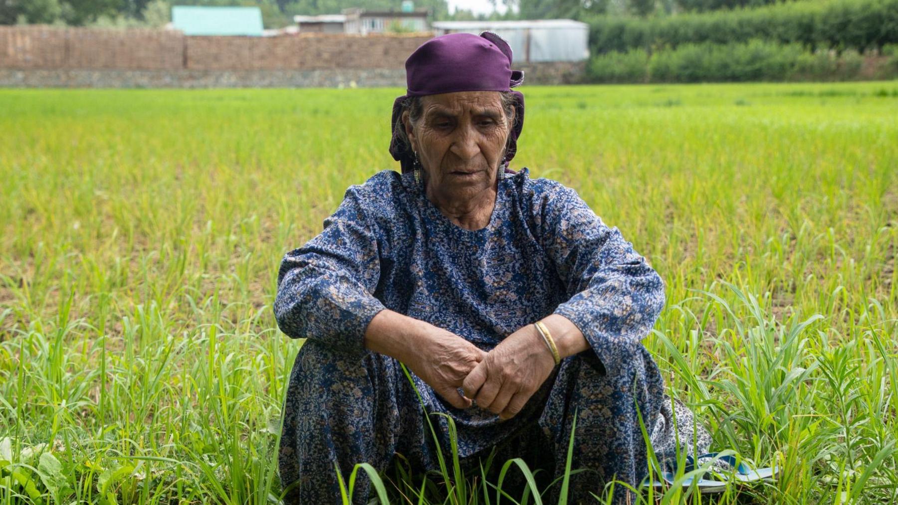 A woman sitting in a field wearing a blue top and a purple scarf