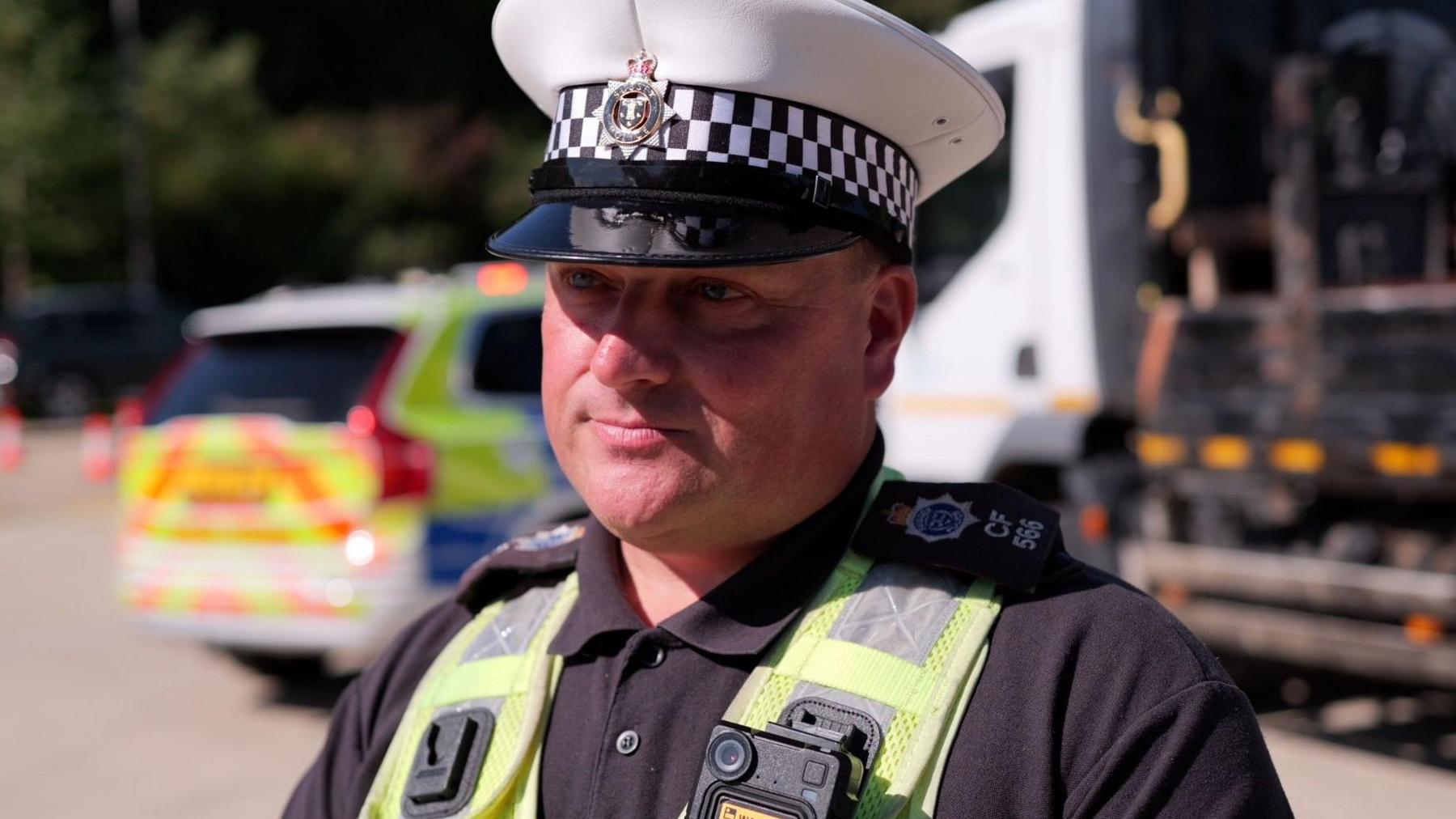 PC Barry Freeman, of the Sussex Police Commercial Vehicle Unit, pictured in front of a heavy goods vehicle and a police car. Both are slightly blurred out.