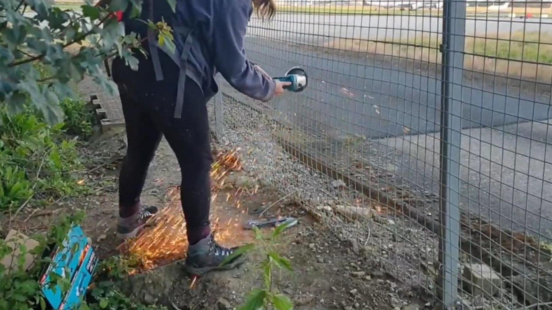 A person cutting through a fence at Stansted Airport using a grinder