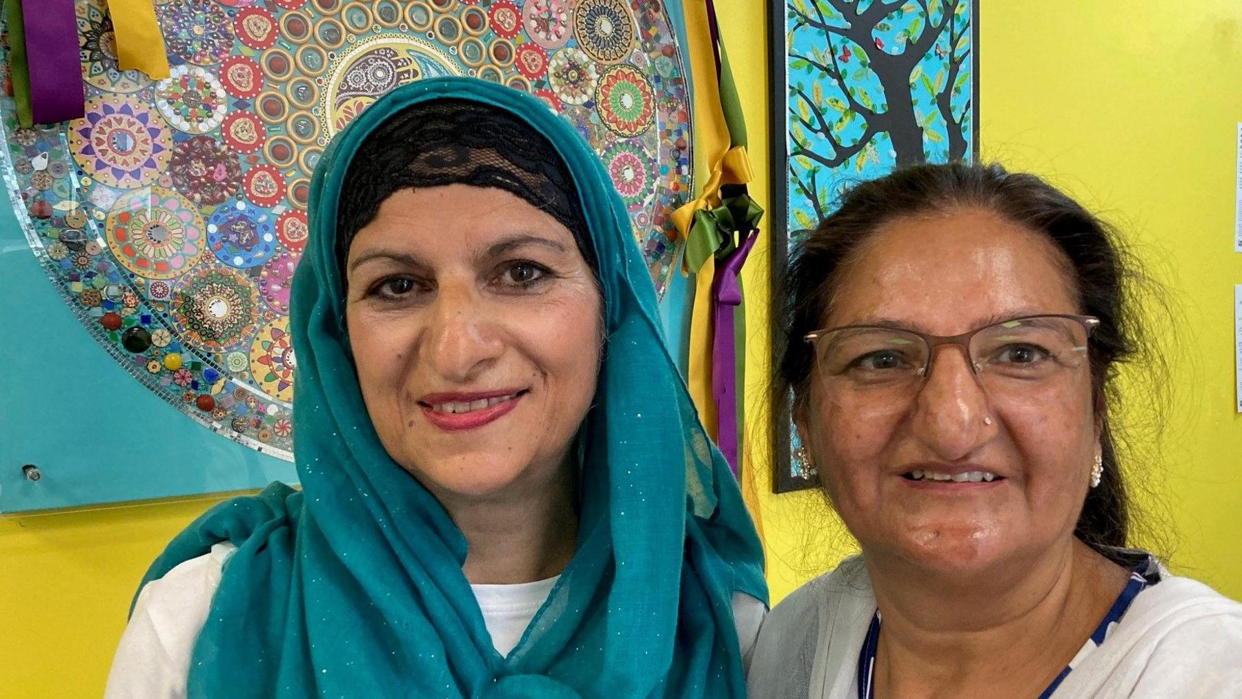 Two women wearing white tops and one who is wearing a turquoise head scarf (al-amira).