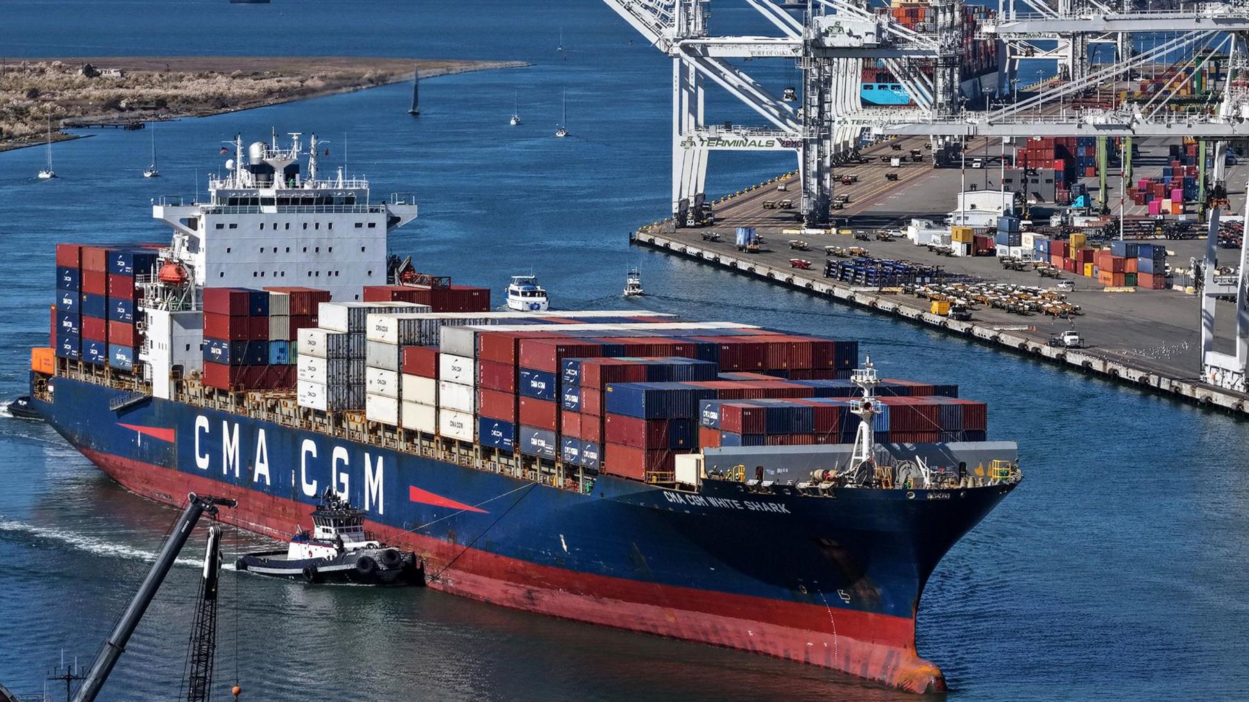 A cargo ship with the letters 'CMA CGM' comes into port with the industrial harbour in the background at the Port of Oakland in October.
