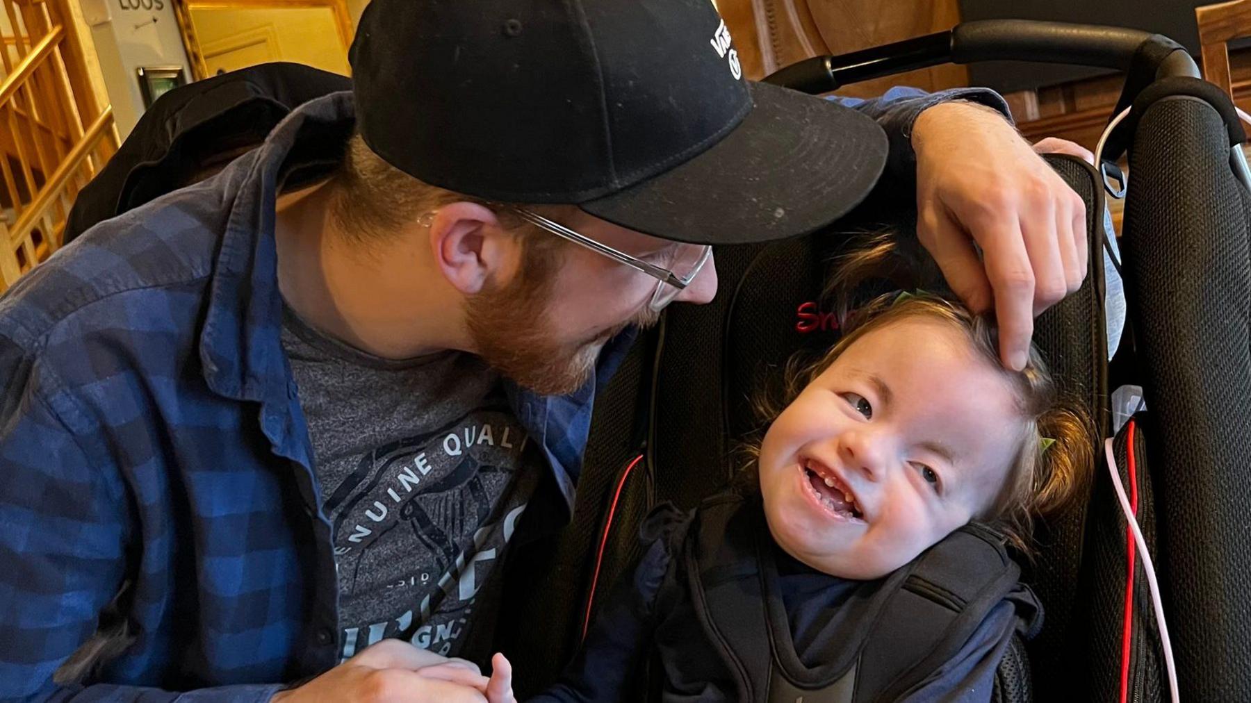 Image of Jack and Ella. Jack is crouched next to Ella in a buggie, leaning over to look at her face. Ella is smiling.