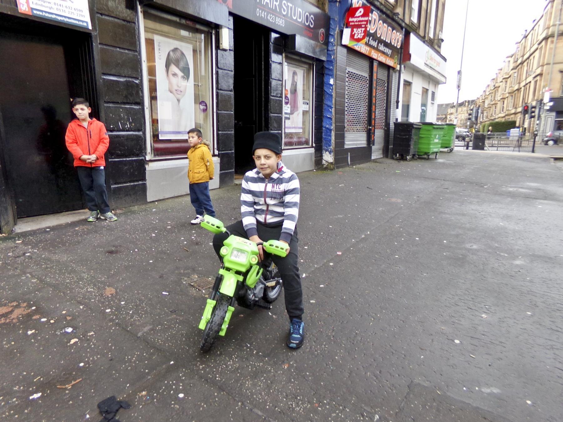 Three boys in the street and one on a green bike
