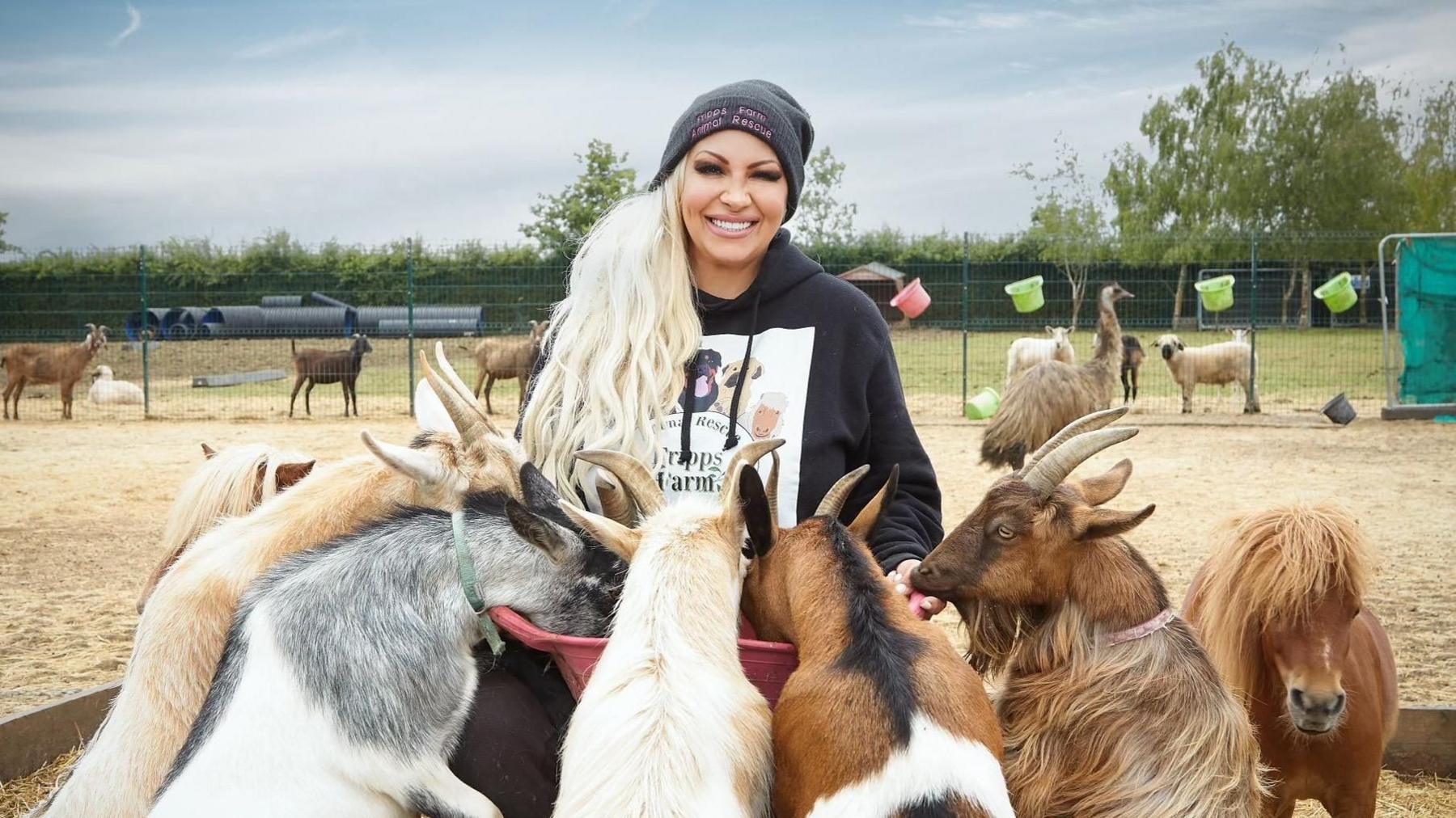 A smiling Jodie Marsh looks directly at the camera as she holds a pink bucket which animals are feeding from