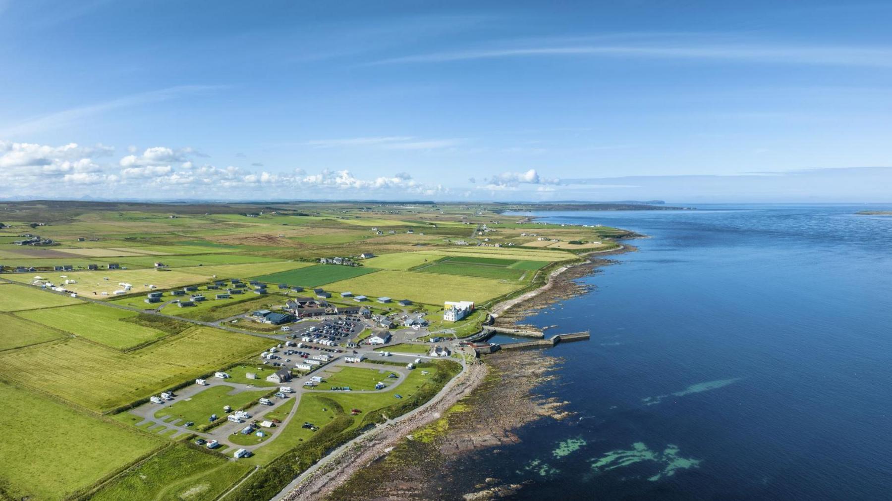 An aerial view of John O' Groats. The community is set in an area of farmland on a shore of the Pentland Firth. It is a sunny day and only a few clouds in the sky.