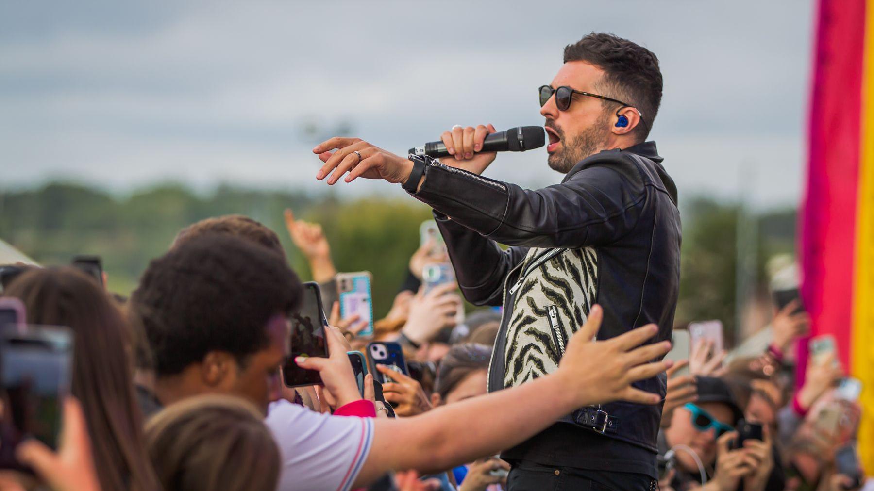 A singer in sunglasses and a leather jacket performs close to a crowd of young fans