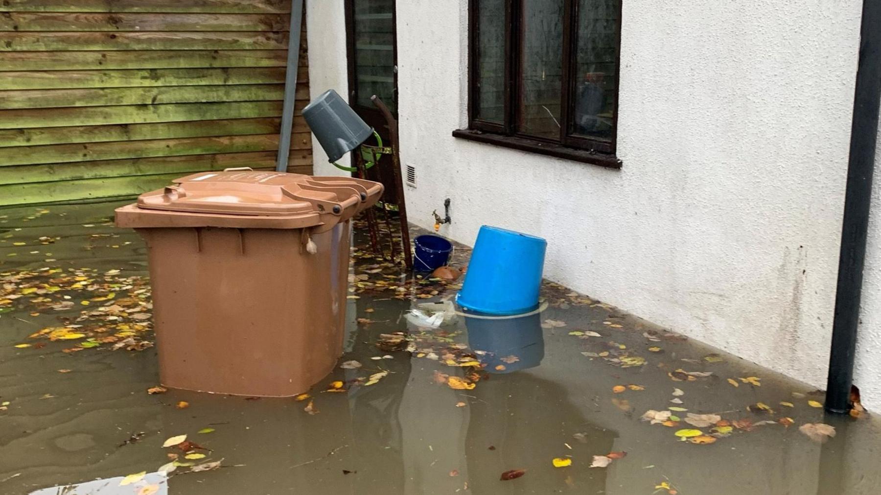 Dirty water half way up the wall of a house and a brown wheelie bin