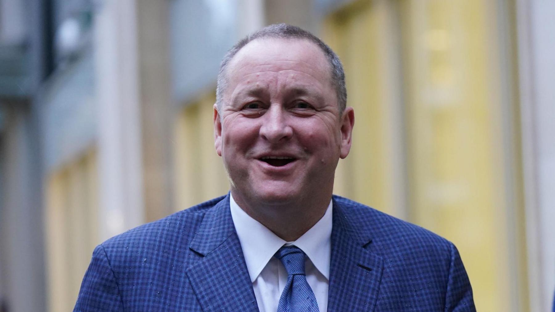 A man with short grey hair smiling at the camera. He is wearing a blue suit and tie with white shirt