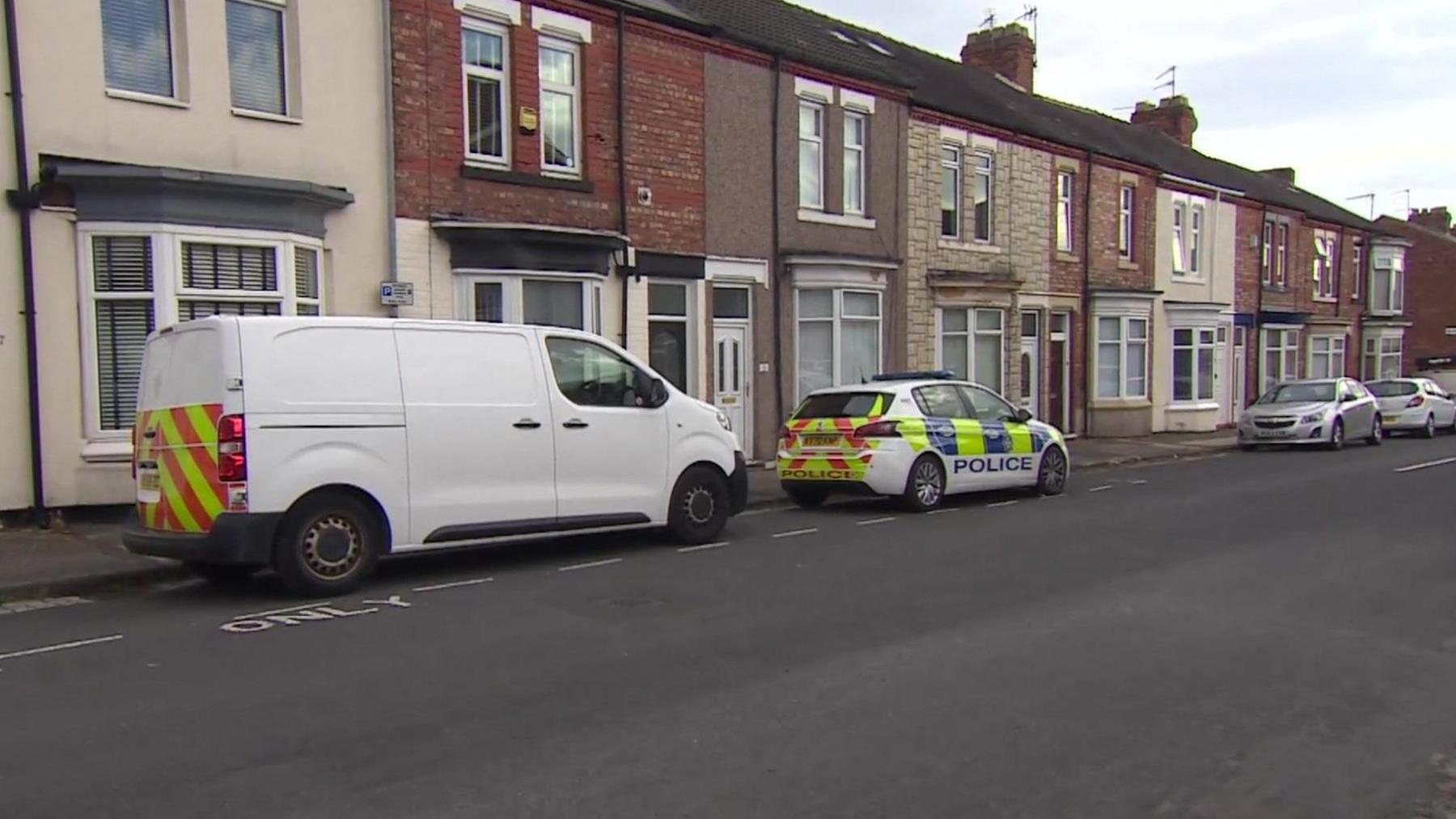 View of a police car and a white van parked on a street of two-storey houses