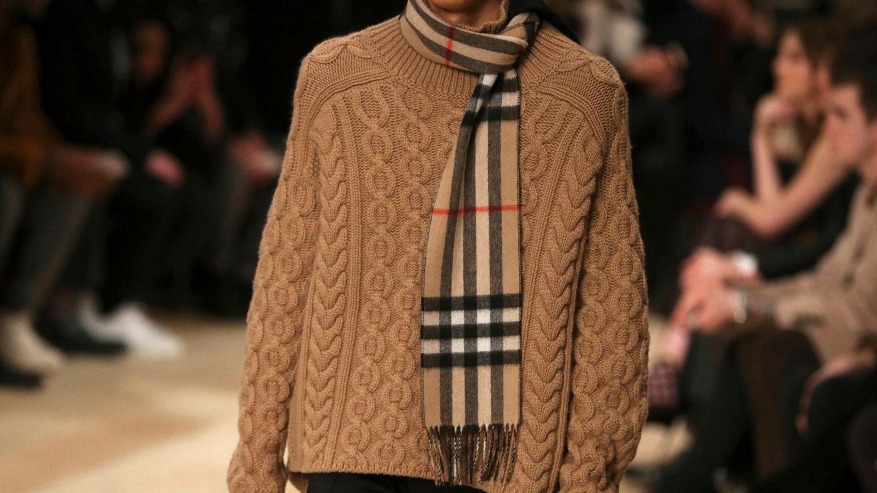 Model on fashion catwalk wearing a beige jumper with a Burberry check scarf