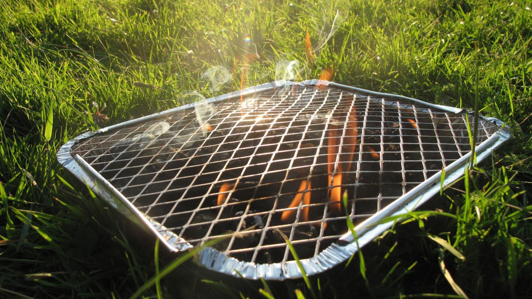 A disposable barbecue smokes on green grass