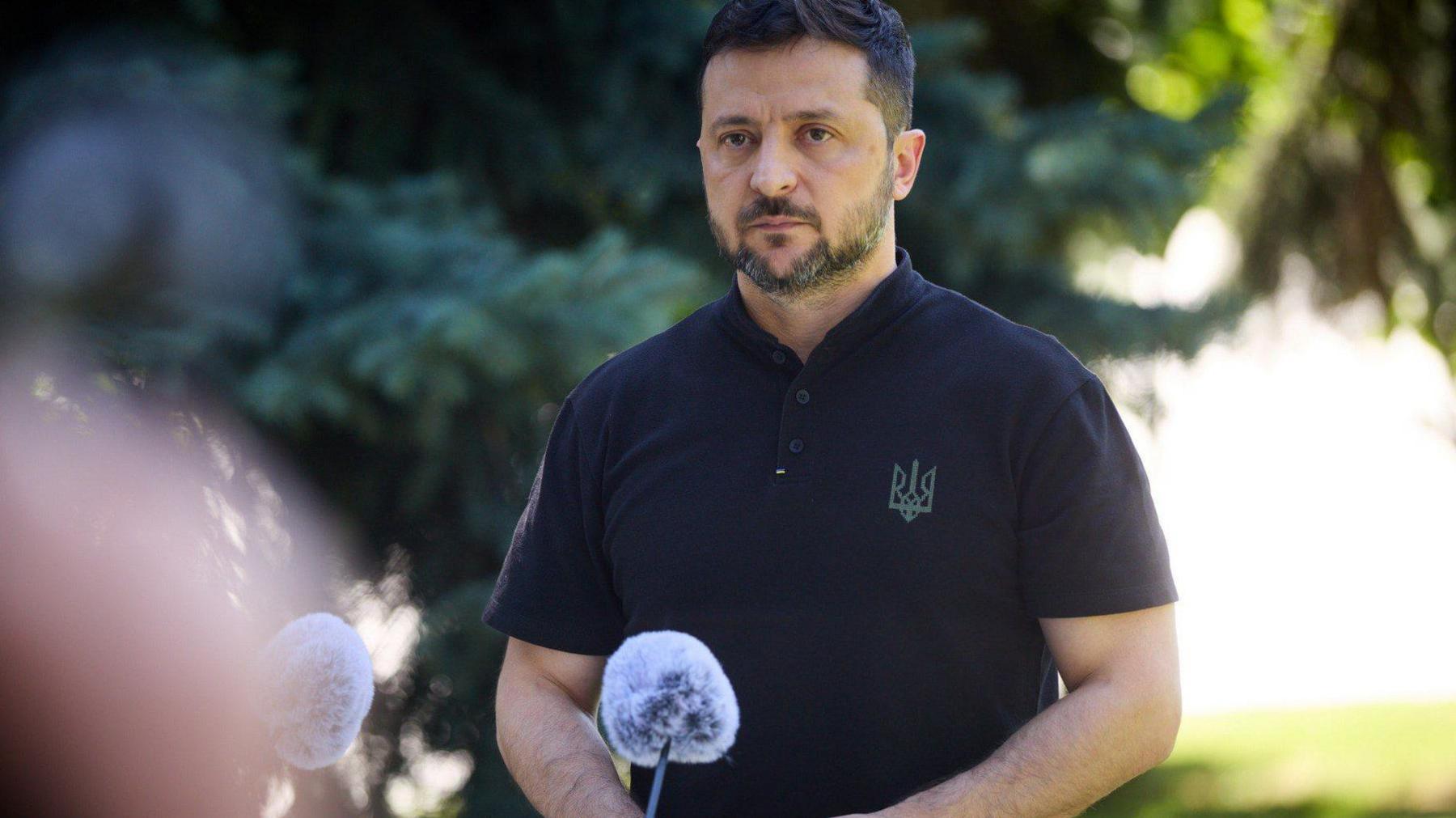 Zelensky, wearing a black polo shirt adorned with the Ukrainian trident looks on as he is photographed in a front of a microphone delivering a press conference outside