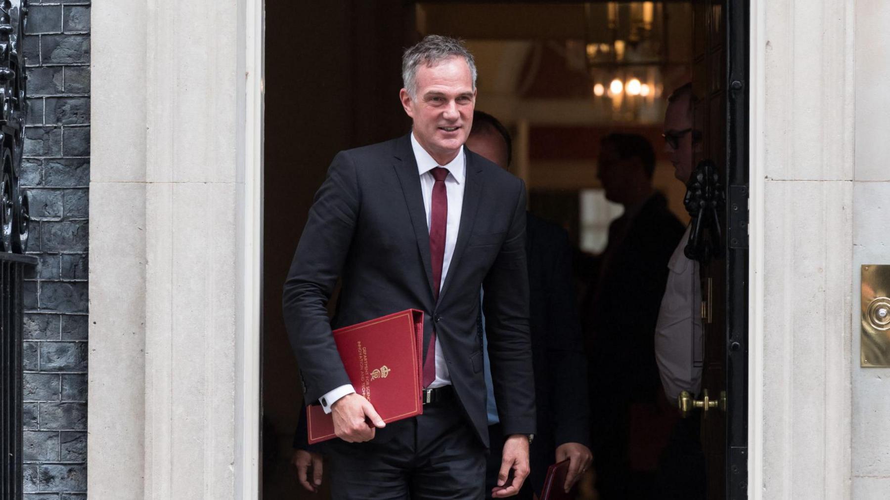 Peter Kyle, a middle aged man, is wearing a suit as he walks out of the doors of Number 10 Downing Street.
