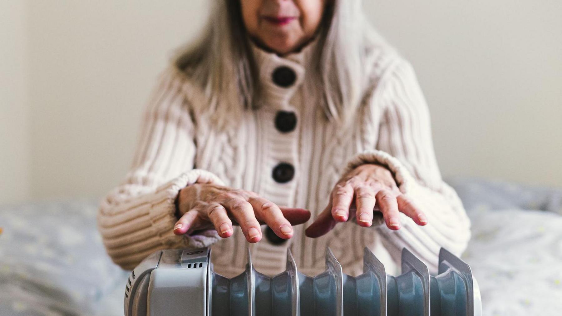 Pensioner warming hands on radiator