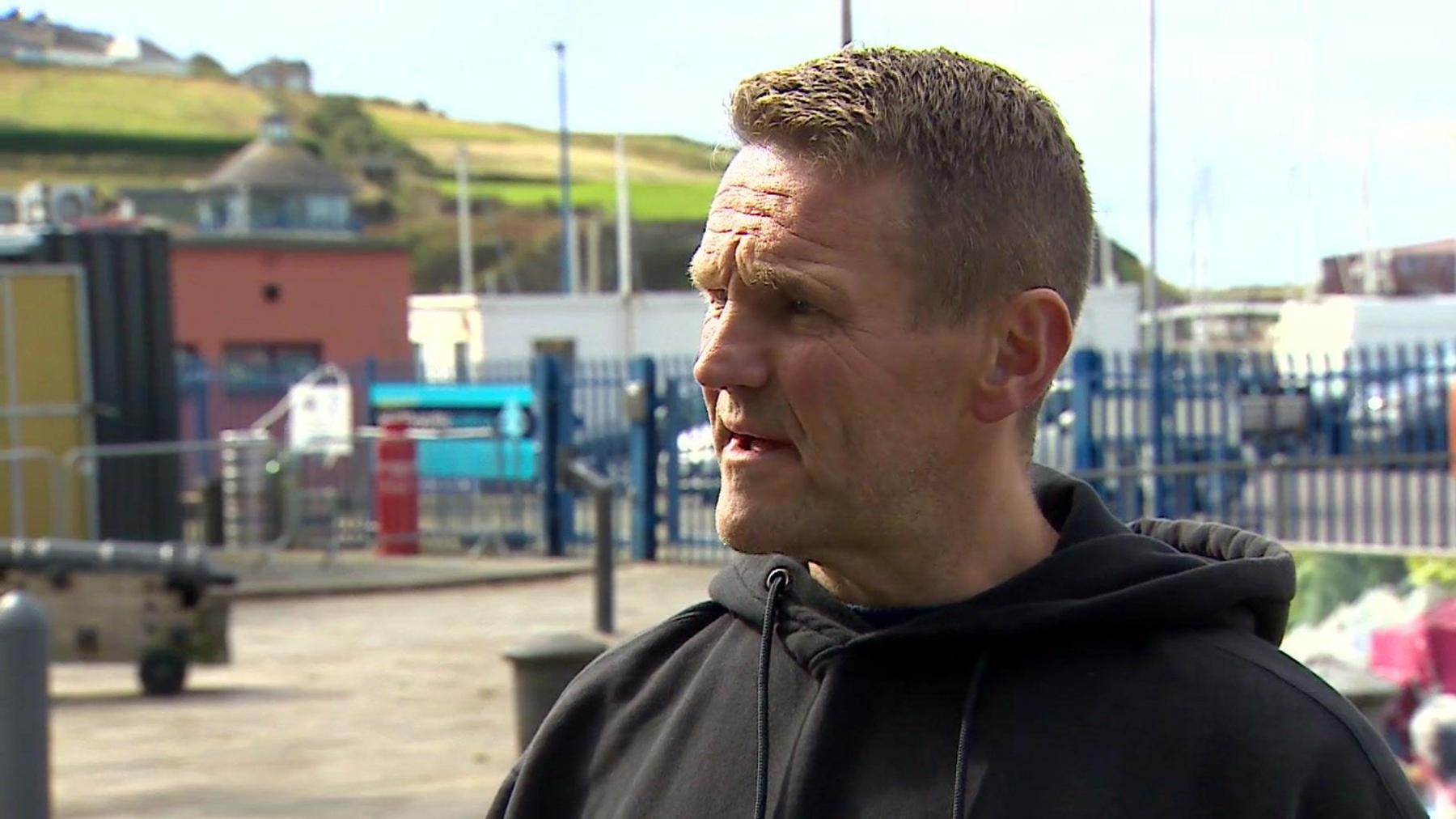 A man in a black hooded top standing at Whitehaven Harbour.