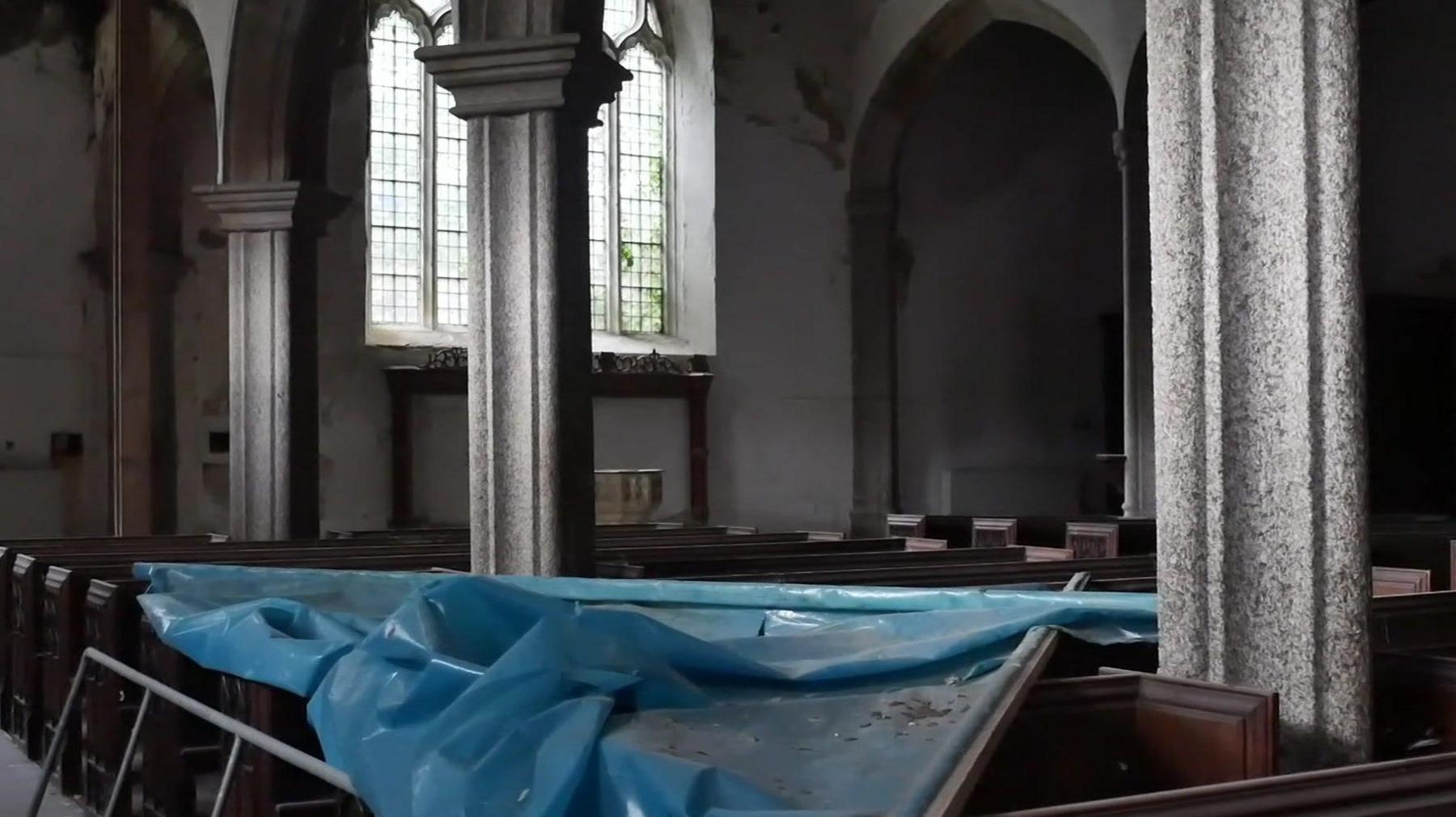 Grey granite columns can be seen inside with a large blue tarpaulin covering several of the wooden pews.