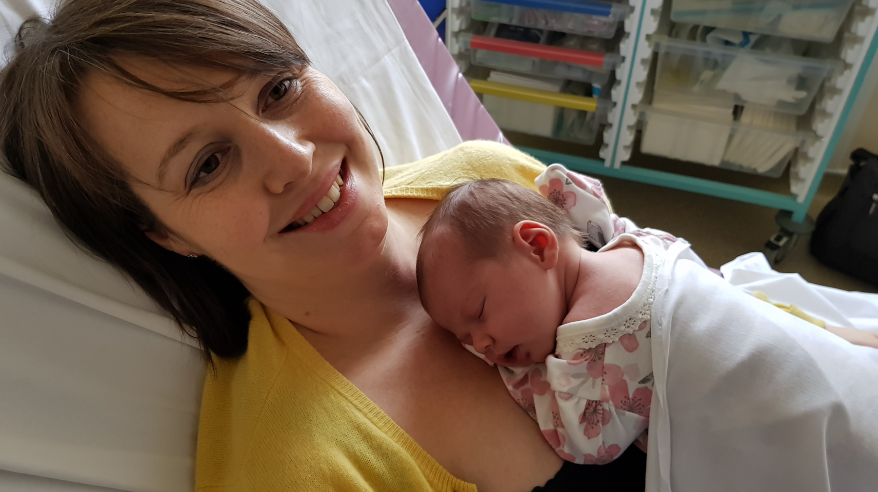 Nicola Wheatley yn gwenu tra'n gorwedd ar wely ysbyty yn dal babi newydd anedig