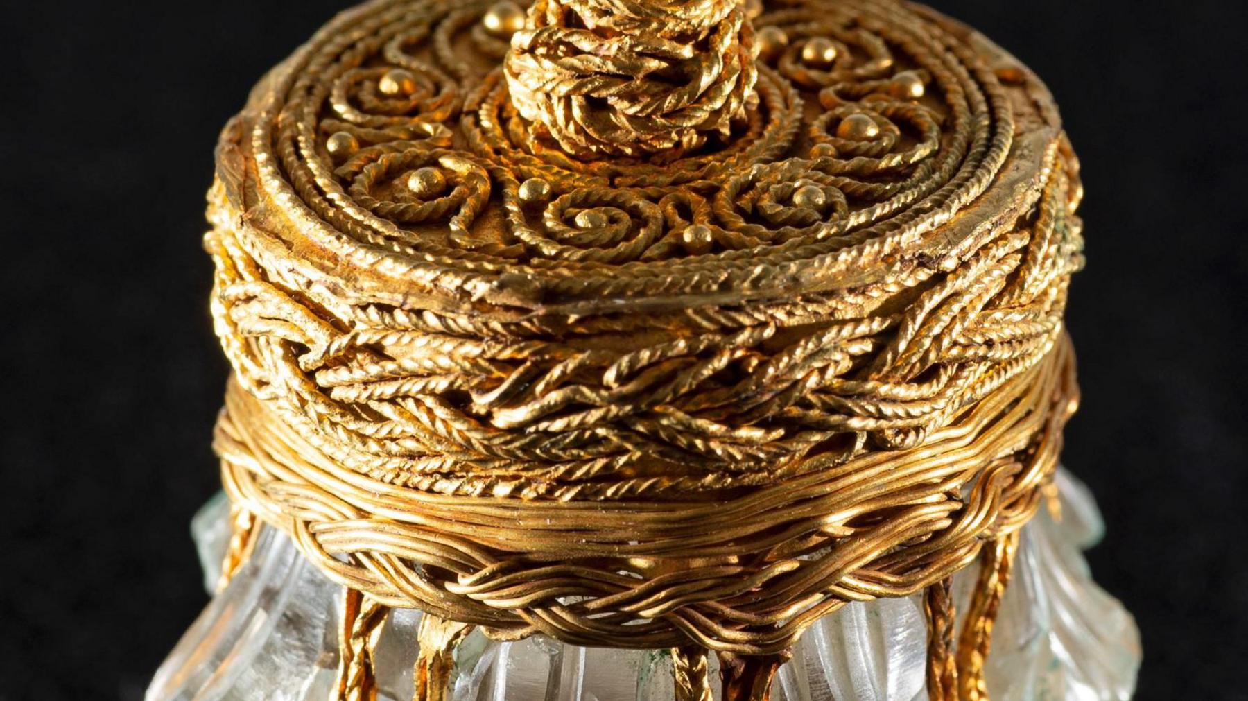 A close-up of the gold embellishments on a rock crystal jar on a black background.