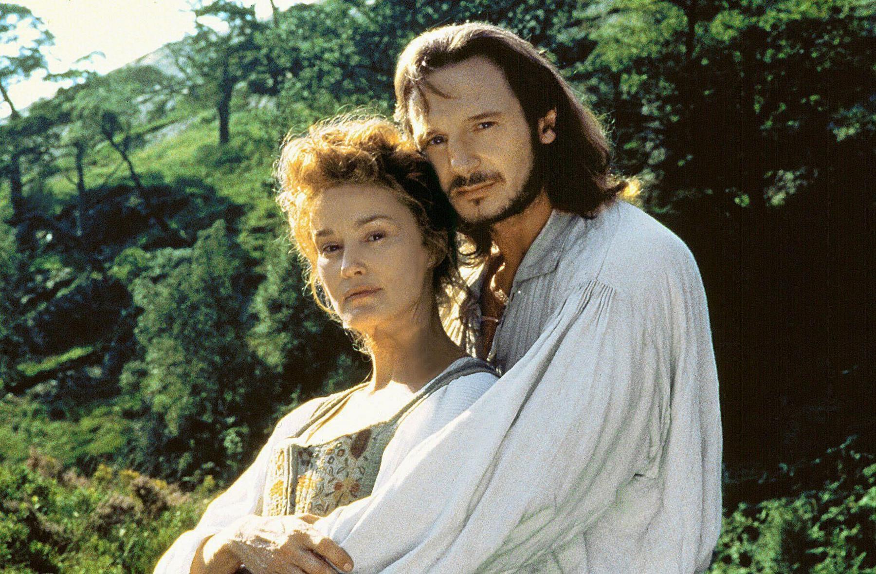 Liam Neeson and Jessica Lange in period costume in Rob Roy. He embraces her from behind and both look to the camera.
