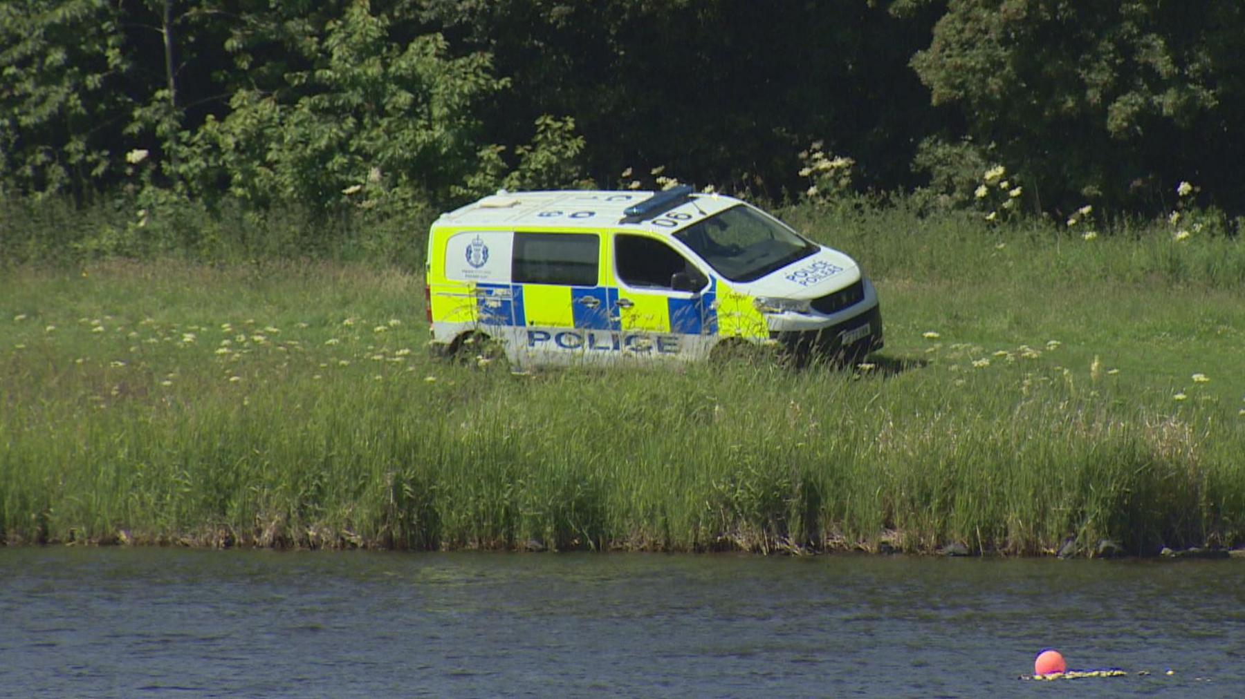 a police van is parked in long grass on the shoreside