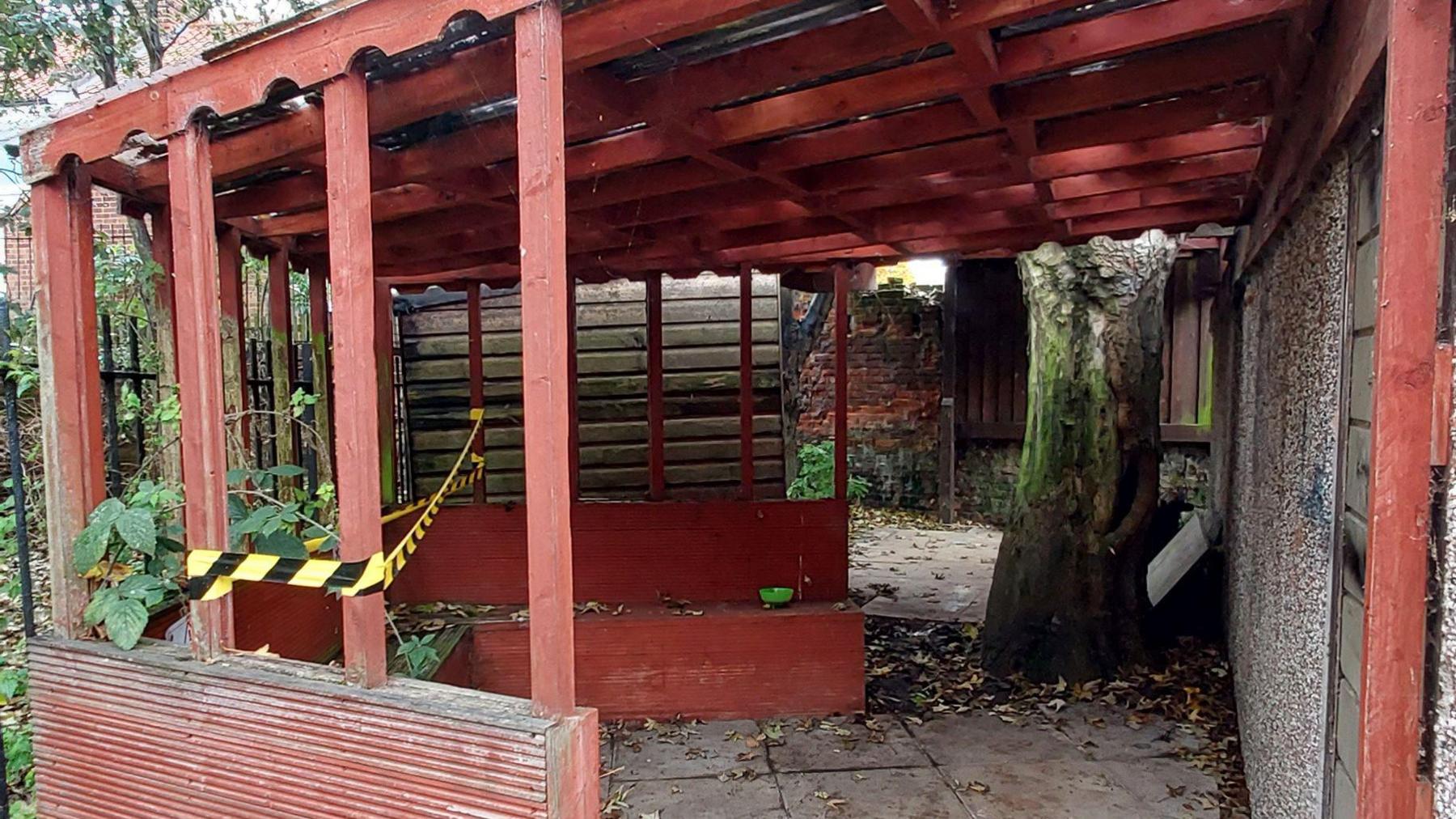 An outdoor space, with wooden structure, with leaves, a tree, a taped off area and 