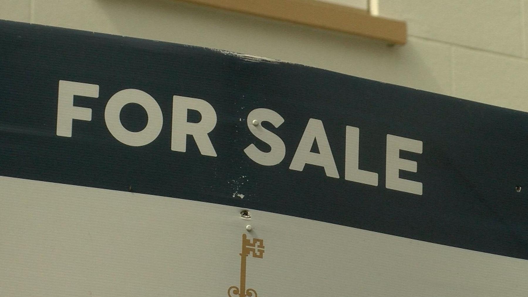 A 'for sale' sign, with white writing on a blue background. The sign is placed outside a property.