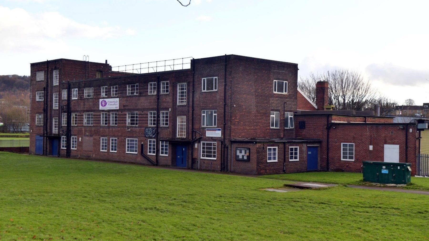 Three-storey brick building on a grassy field.