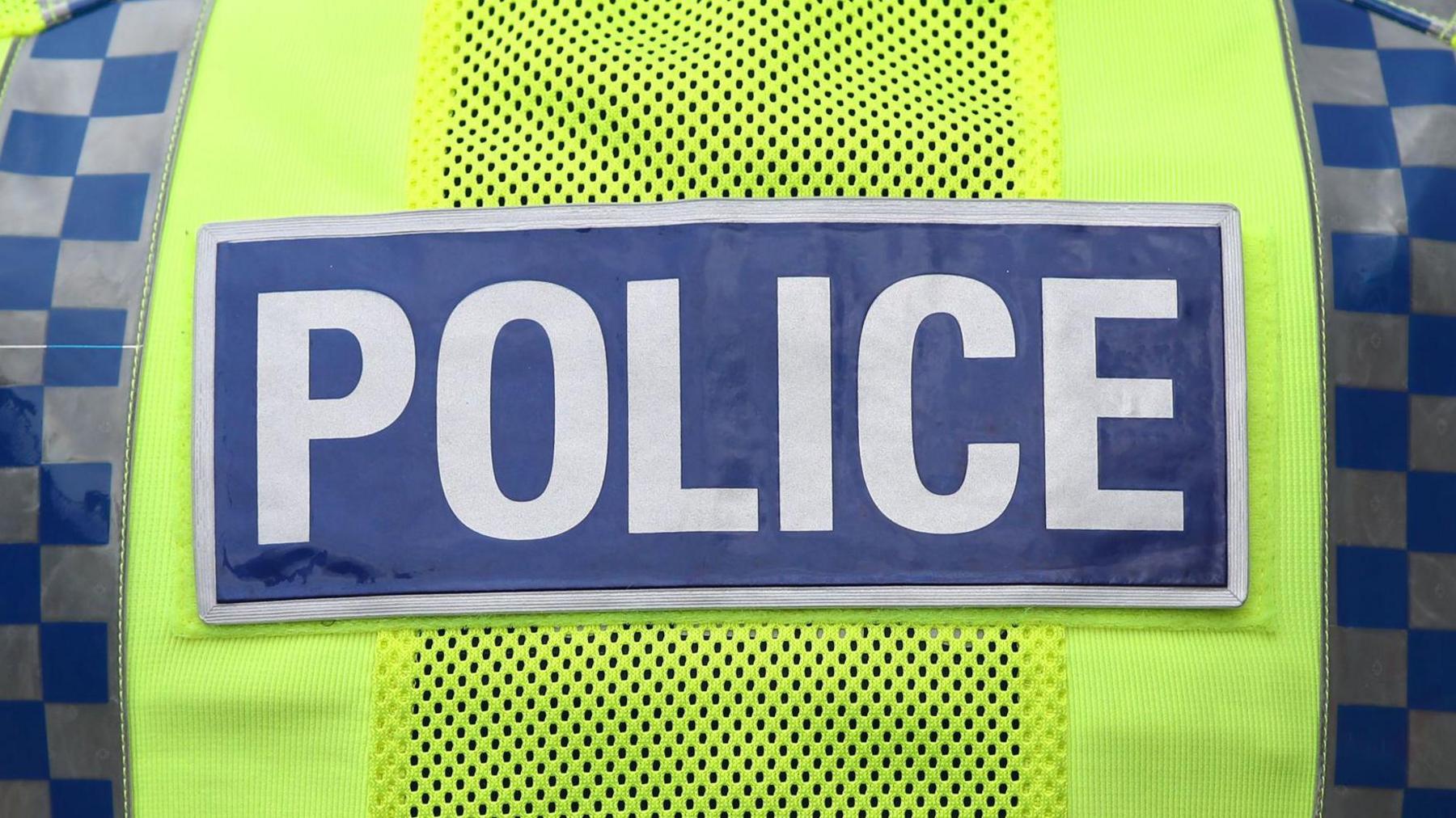 A yellow-green hi-vis jacket with the word 'police' written in silver letters on a blue background