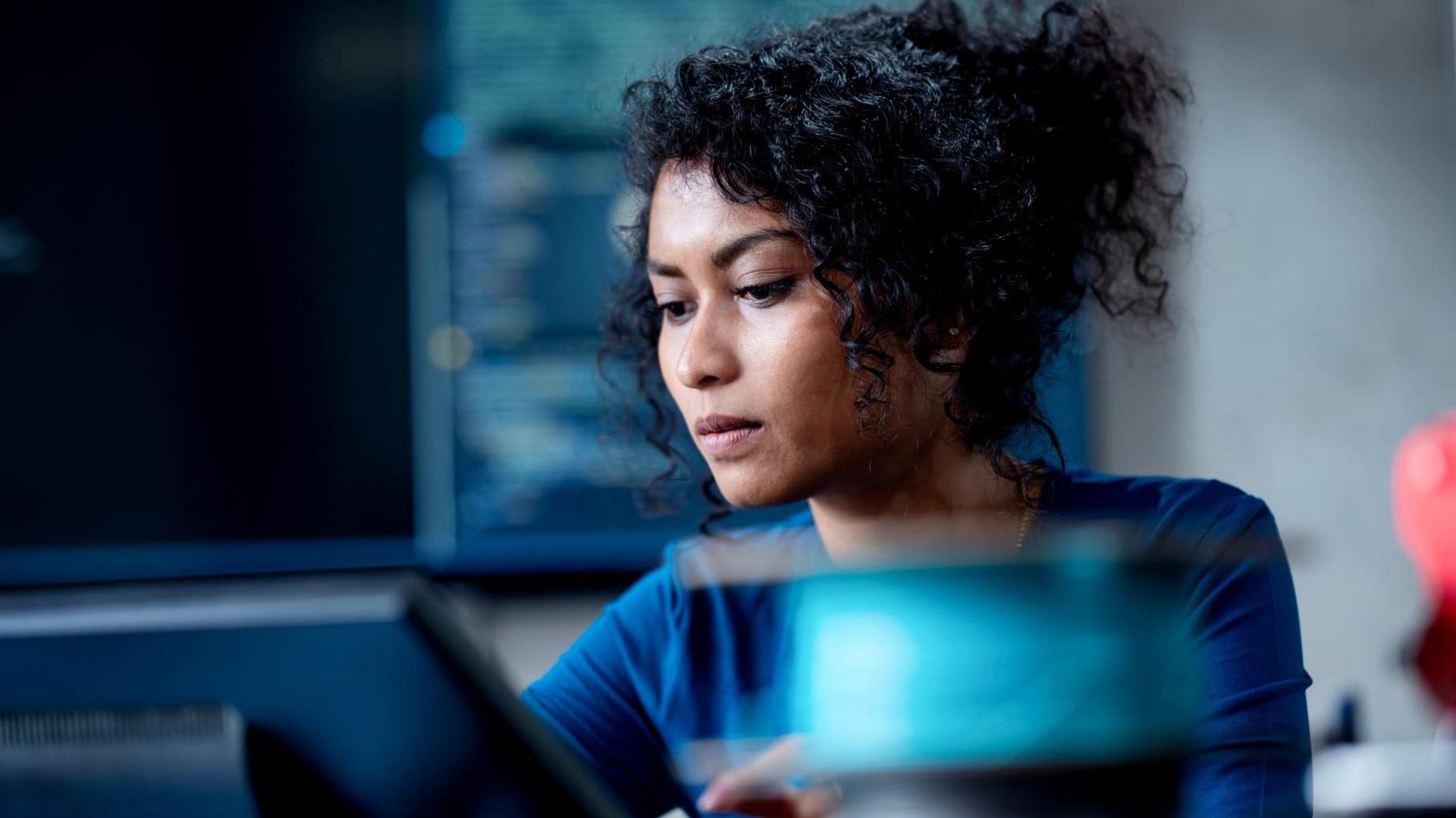 A young woman with a slightly concerned look on her face sitting in an office, looking down at a computer.