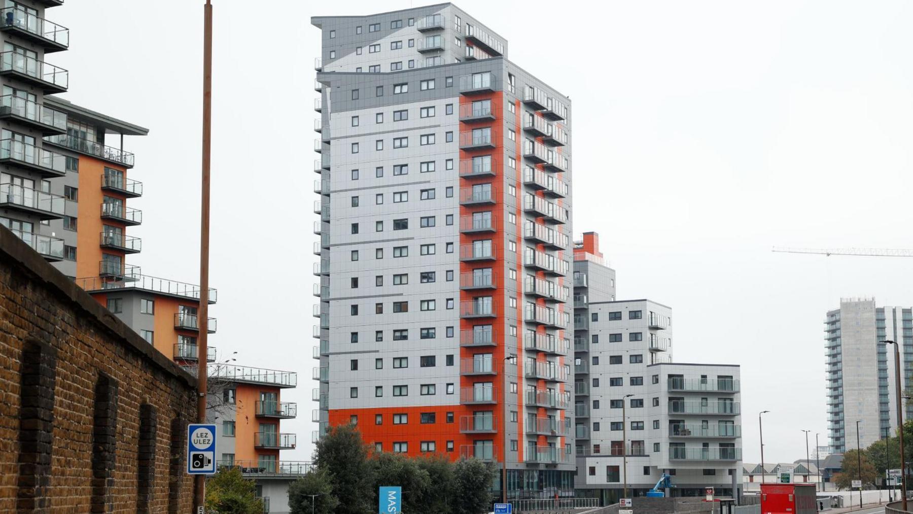 The large grey tower has a bright orange stripe down the side and along the bottom. The are other grey towerblocks in the distance. 