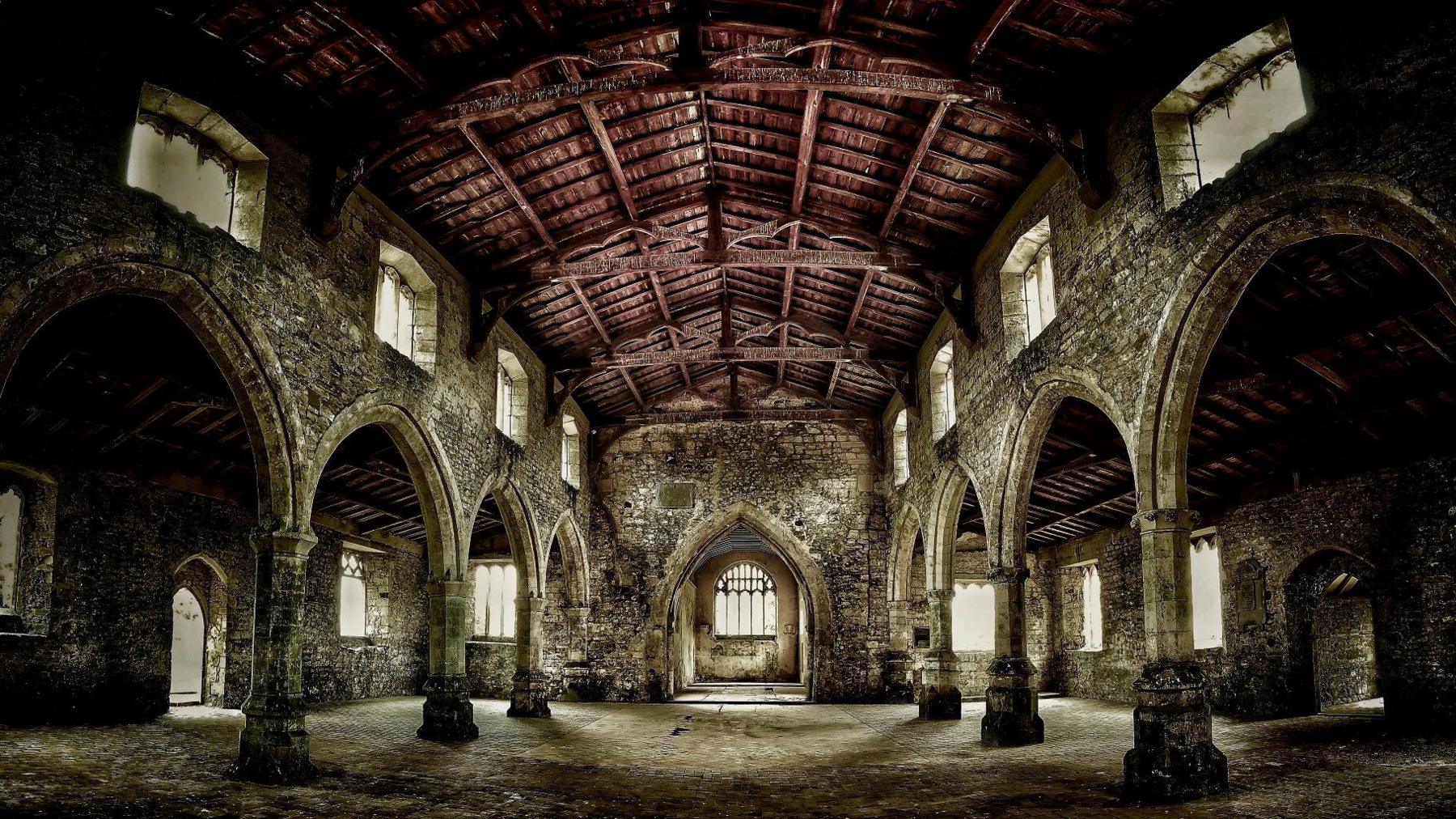 The atmospheric interior of a medieval church with elegant arches and arcades of brick and stone beneath a wooden roof.