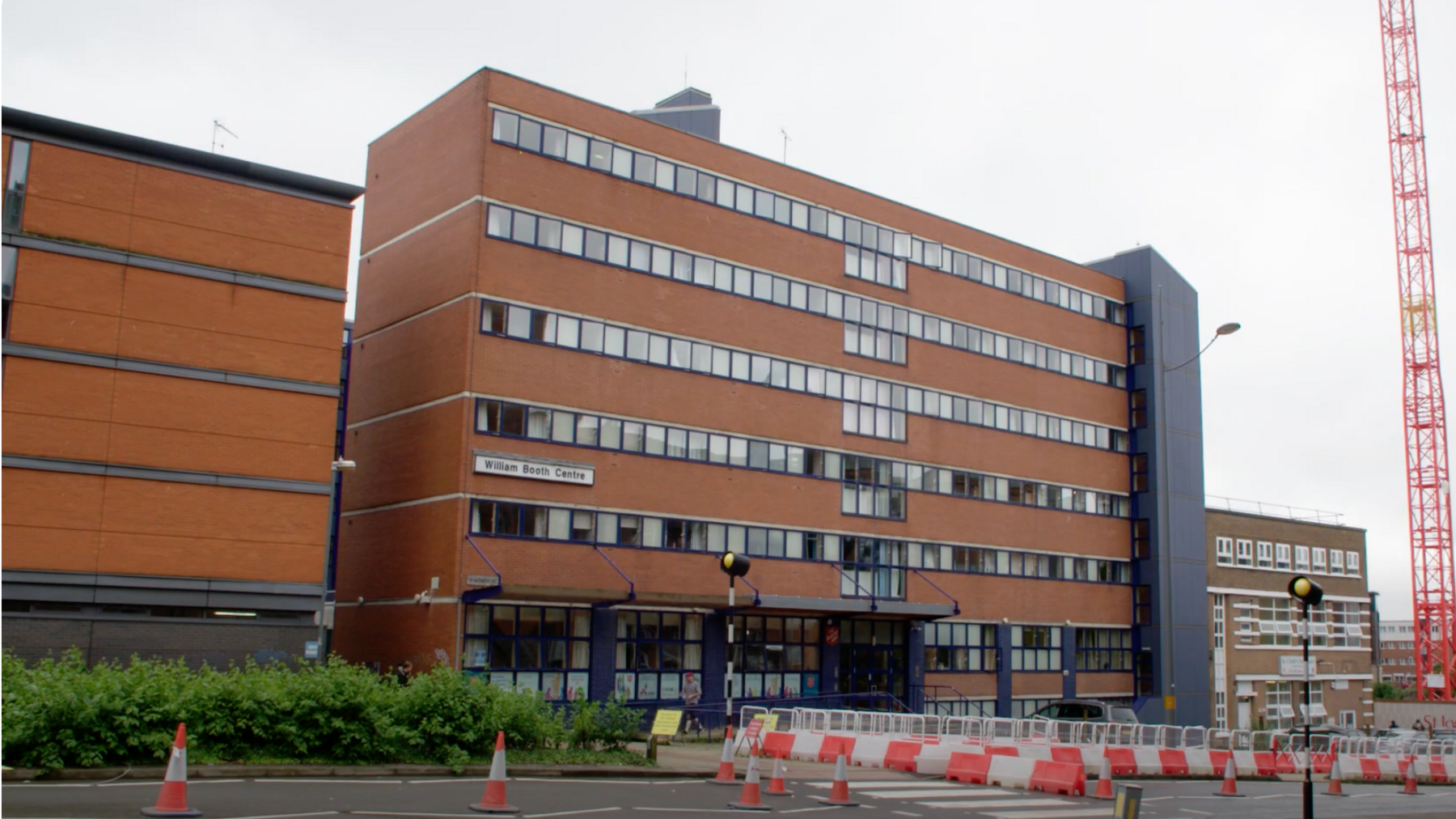 Six-storey, red brick building, with sign reading William Booth Centre on the left-hand side. Roadworks with cones and fencing taking place in-front of the building.