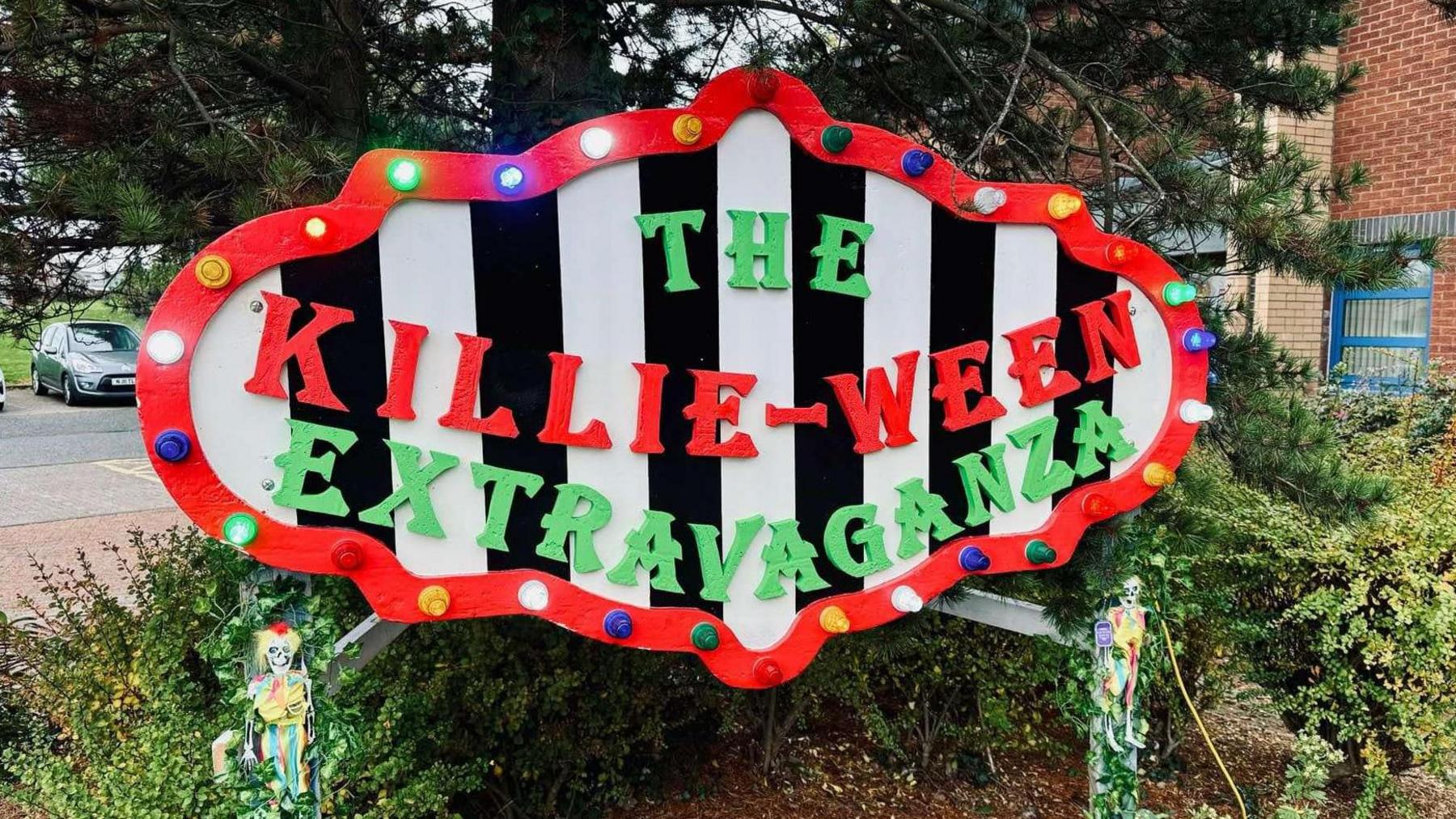 A black and white striped sign with text THE KILLIE-WEEN EXTRAVAGANZA in red and green. 