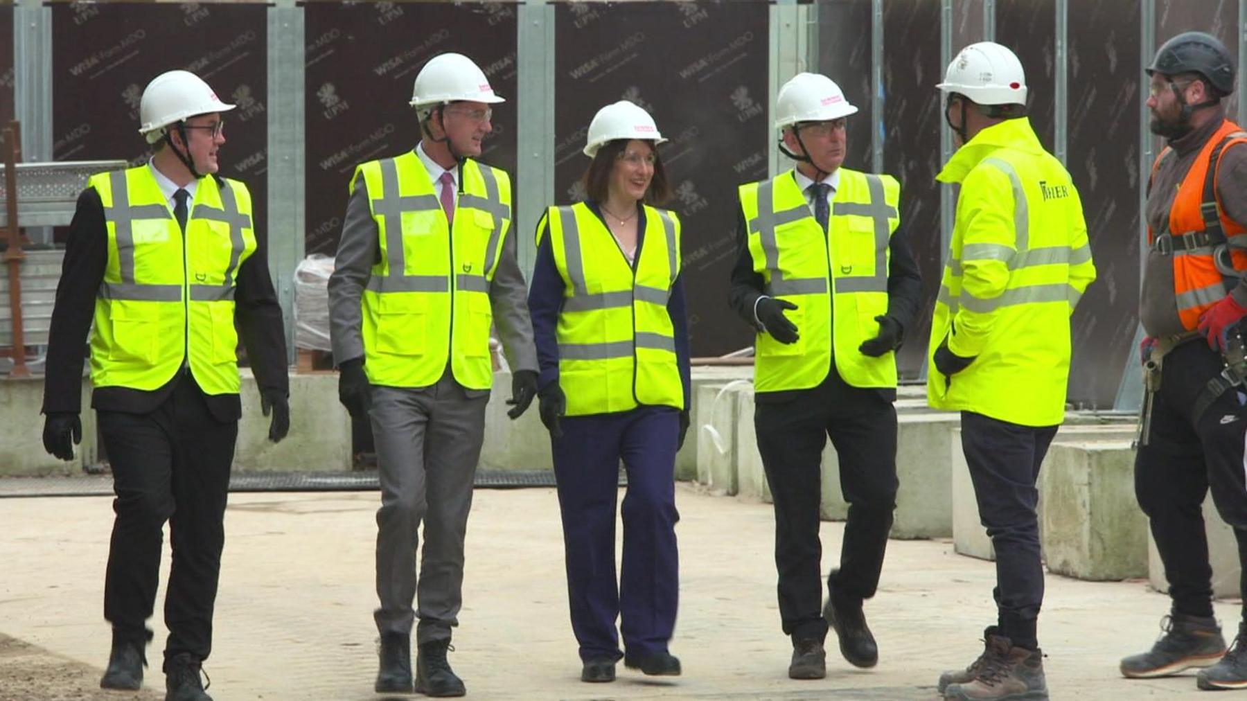 Rachel Reeves in the centre of the picture with men on either side of her. They are all wearing hi-vis jackets and helmets.