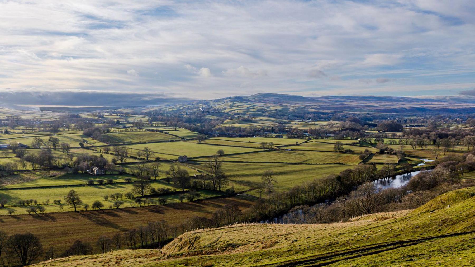 A river with fields, trees and hills beyond.