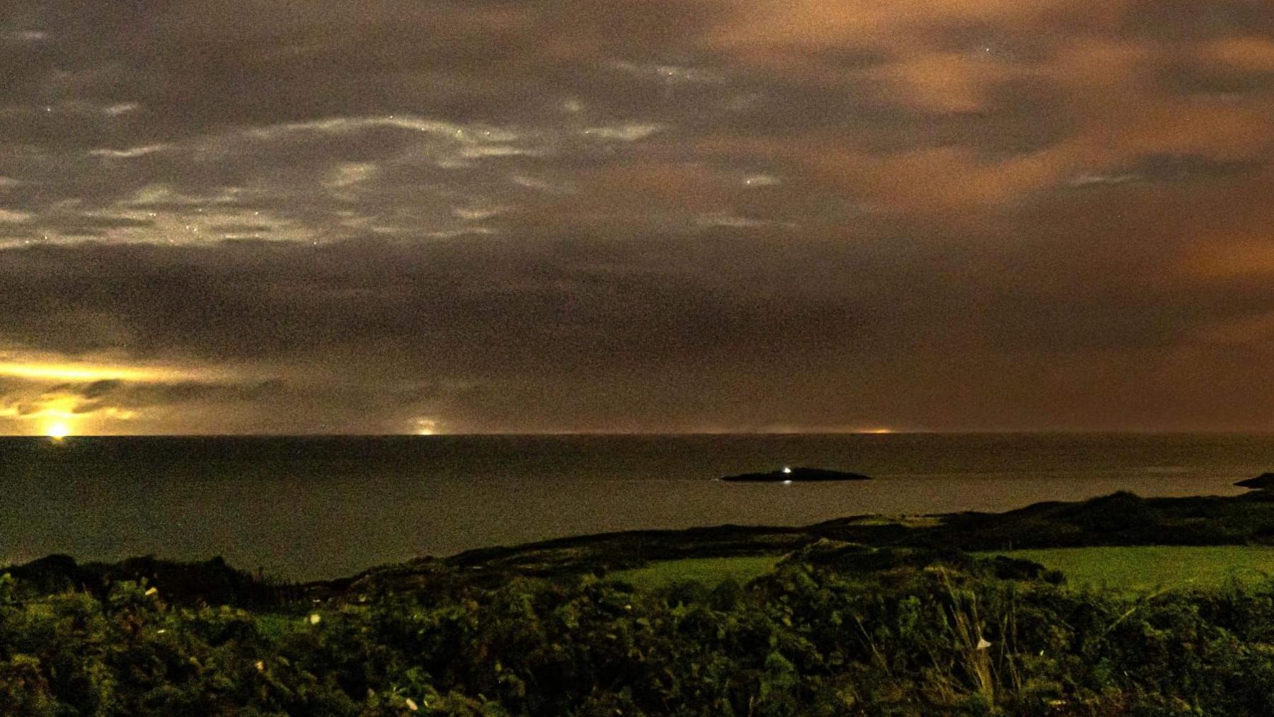 A photo from the town of Amlwch looking out to the sea with East Mouse in the distance and a light held by Di Mills shining from it