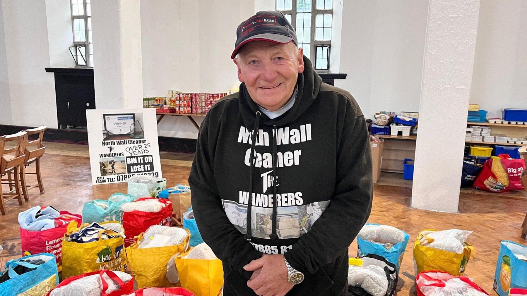 Frank Sparkes, wearing a black hooded top, surrounded by bags containing winter essentials 