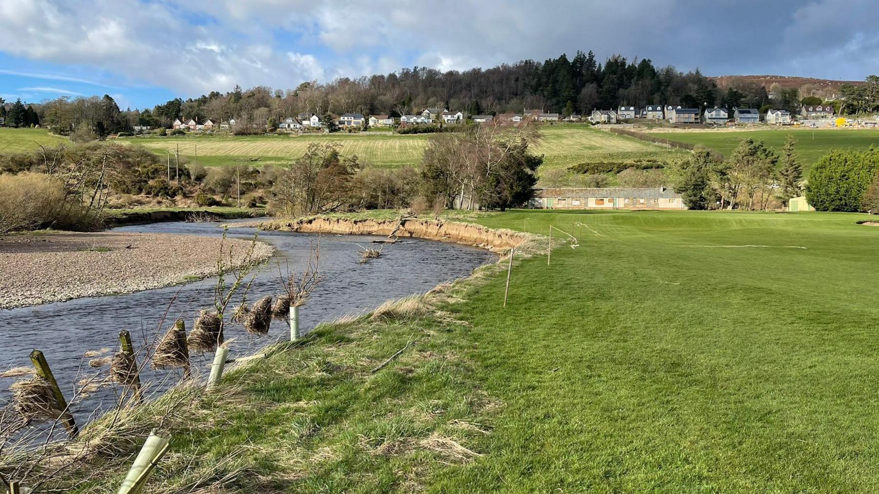 A picture of a golf course with a line of barbed wire hanging across the river 