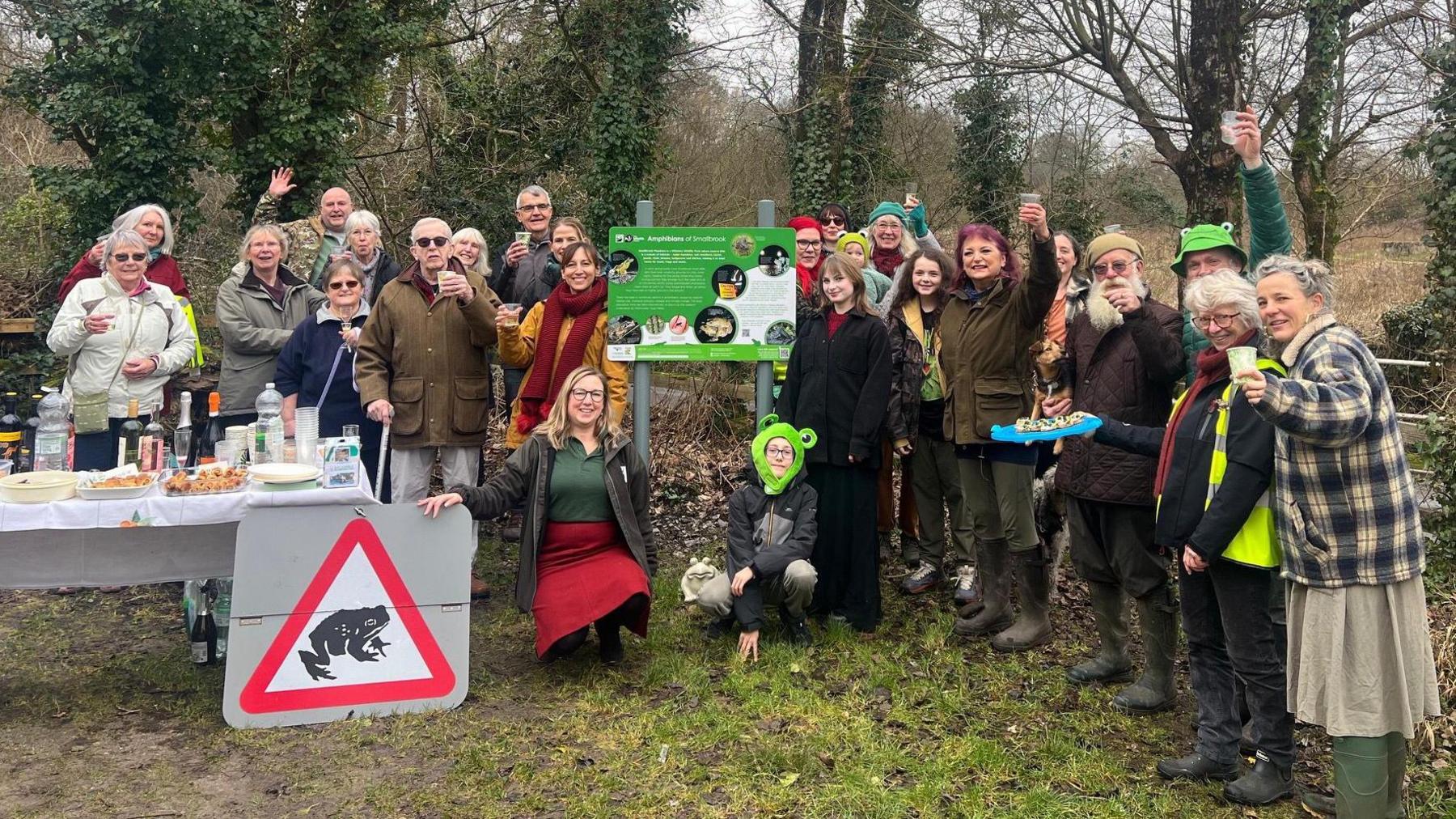 Picture of Toad Patrol volunteers lined up to celebrate the closure of Smallbrook Road. There is a sign which includes a picture of a toad and several people are wearing toad hats.