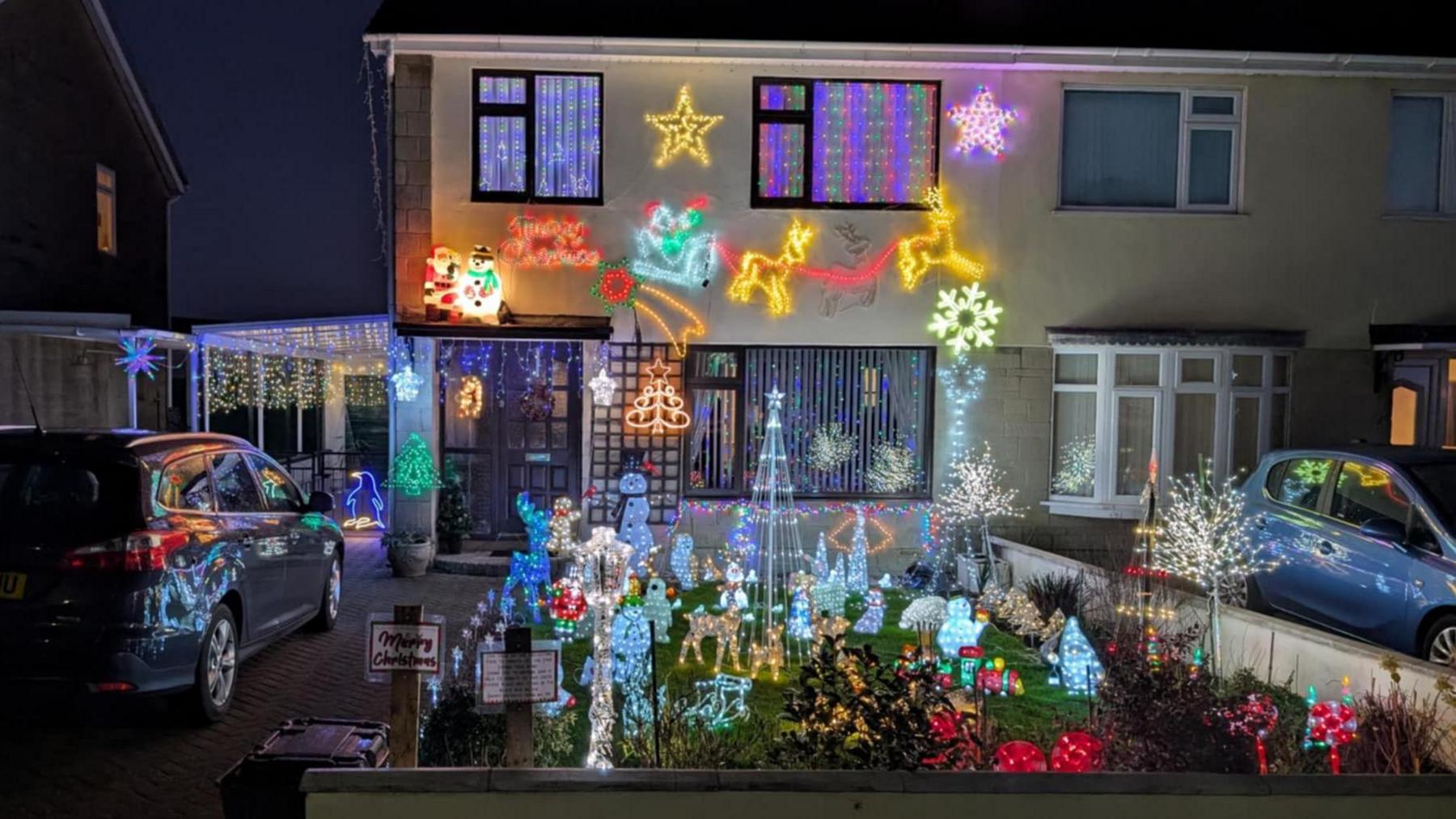 Christmas display in Frome. The house is covered in lights such as stars and a sleigh. The front garden features other light figures like trees, reindeers and penguins. 