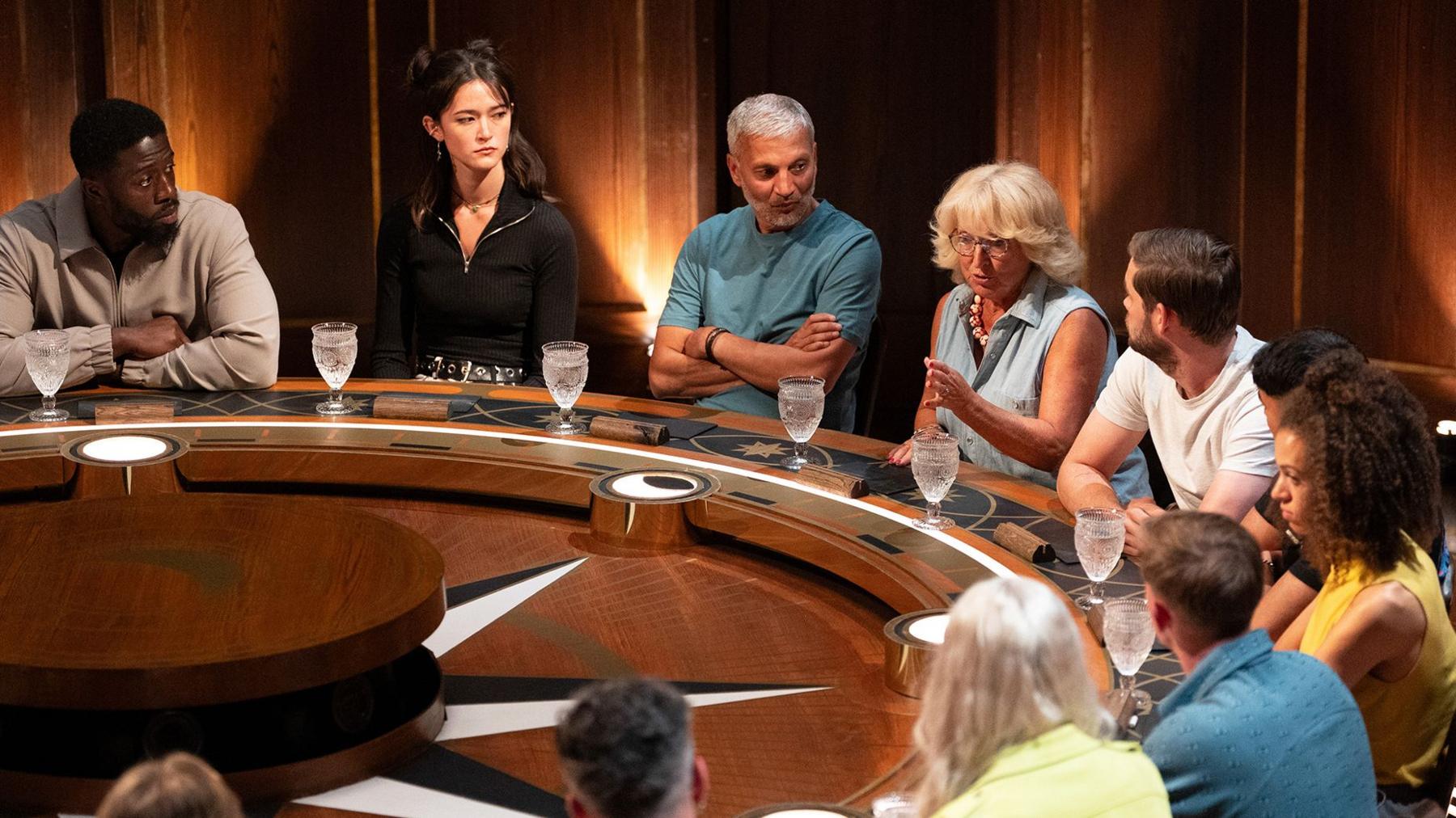 Traitors from the BBC TV series 4 sit at the round table. The focus is on Traitor Fiona who is speaking to the rest of the group
