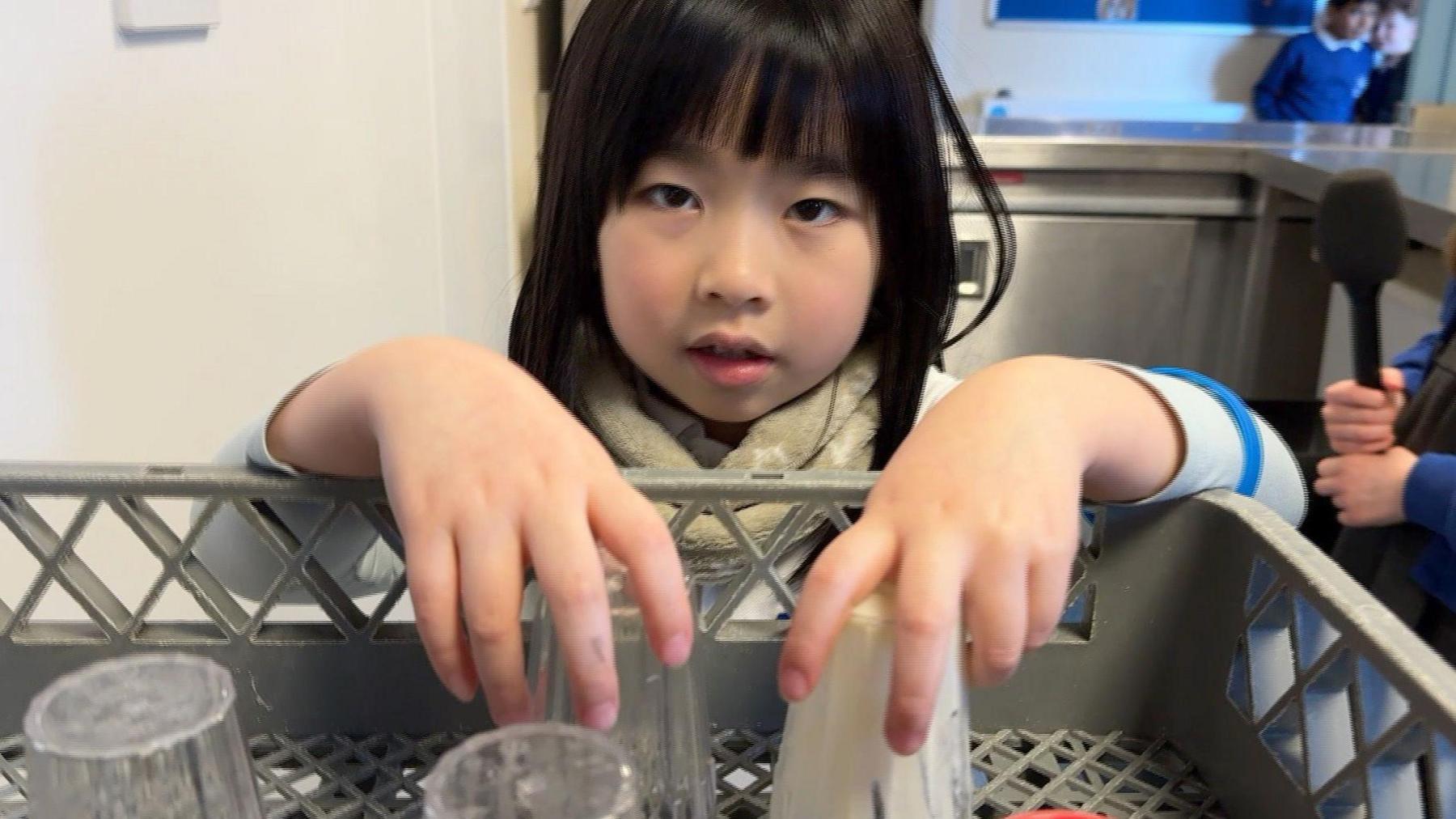 A young girl placing plastic pots into a dishwasher to be washed and reused