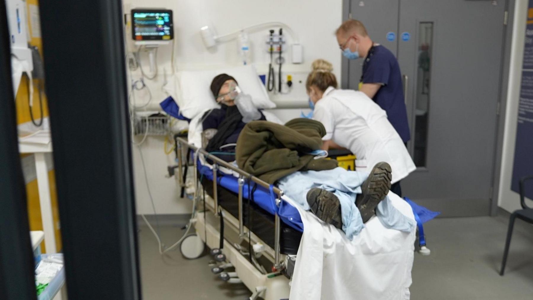 A patient lays in a hospital bed with nurses tending to him slightly out of focus