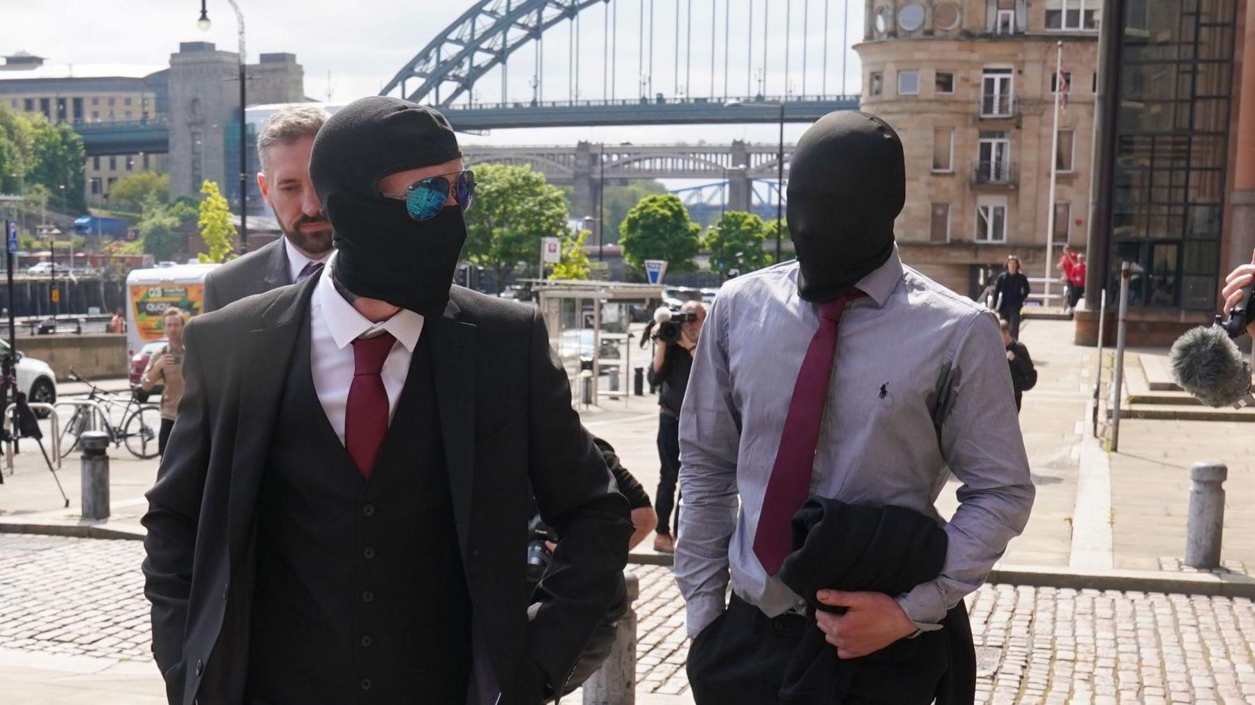 Adam Carruthers and Daniel Graham are walking into court and are smartly dressed in suits with a tie but also wearing balaclavas and sunglasses